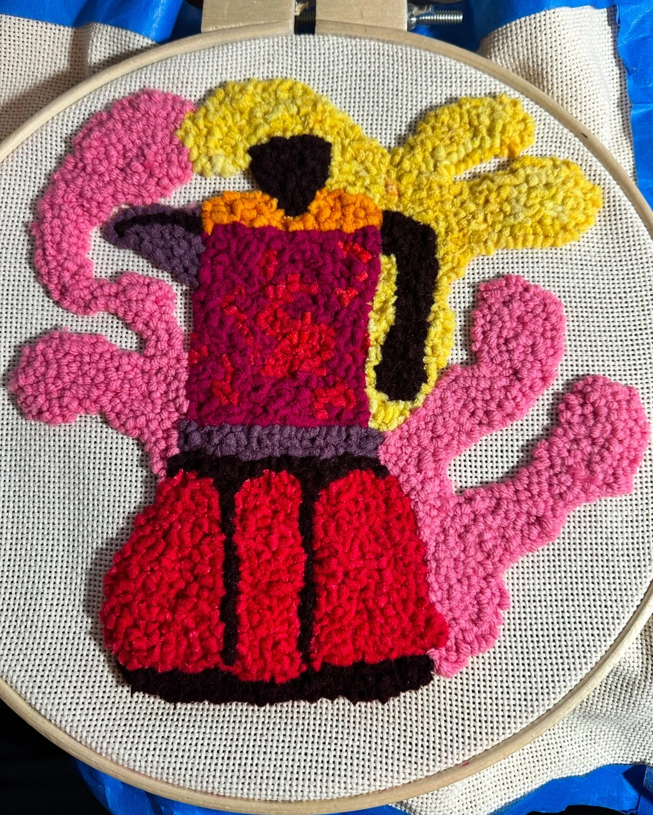 A colorful needlepoint rug design framed in a circular embroidery hoop.