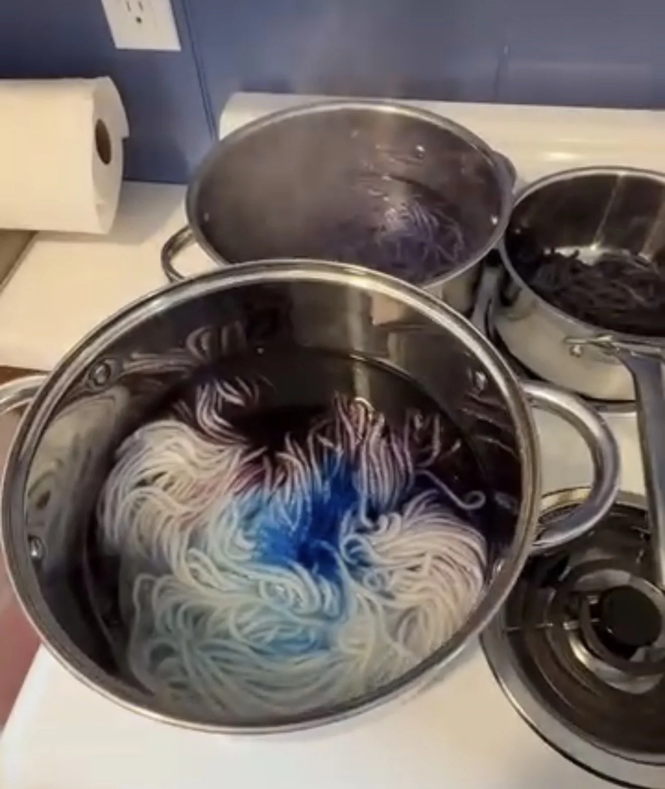 Cooking pots with boiling yarn on a stove, with a roll of paper towels nearby.