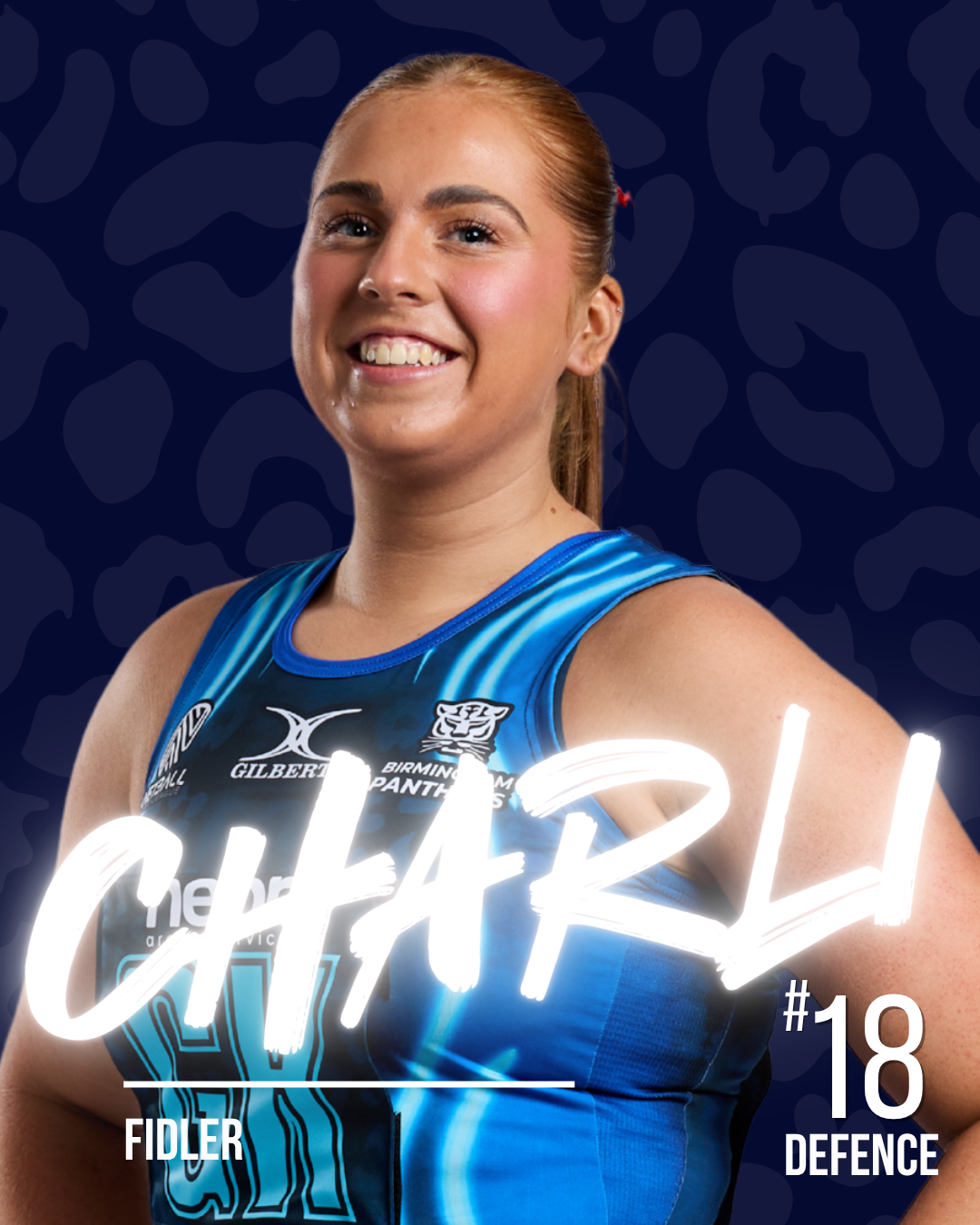 A netball player in a blue netball dress, smiling with her hair tied back, standing against a dark blue patterned background.