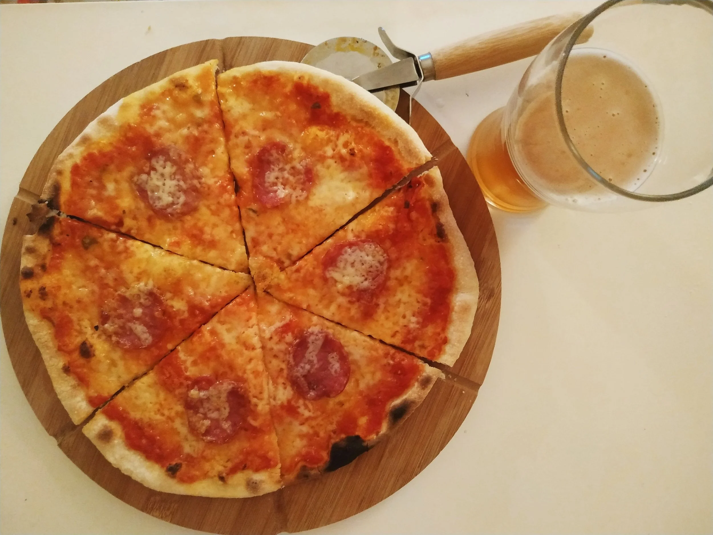 A thin-crust pizza topped with tomato sauce, mozzarella, and spicy sausage, served on a wooden board beside two glasses of beer.