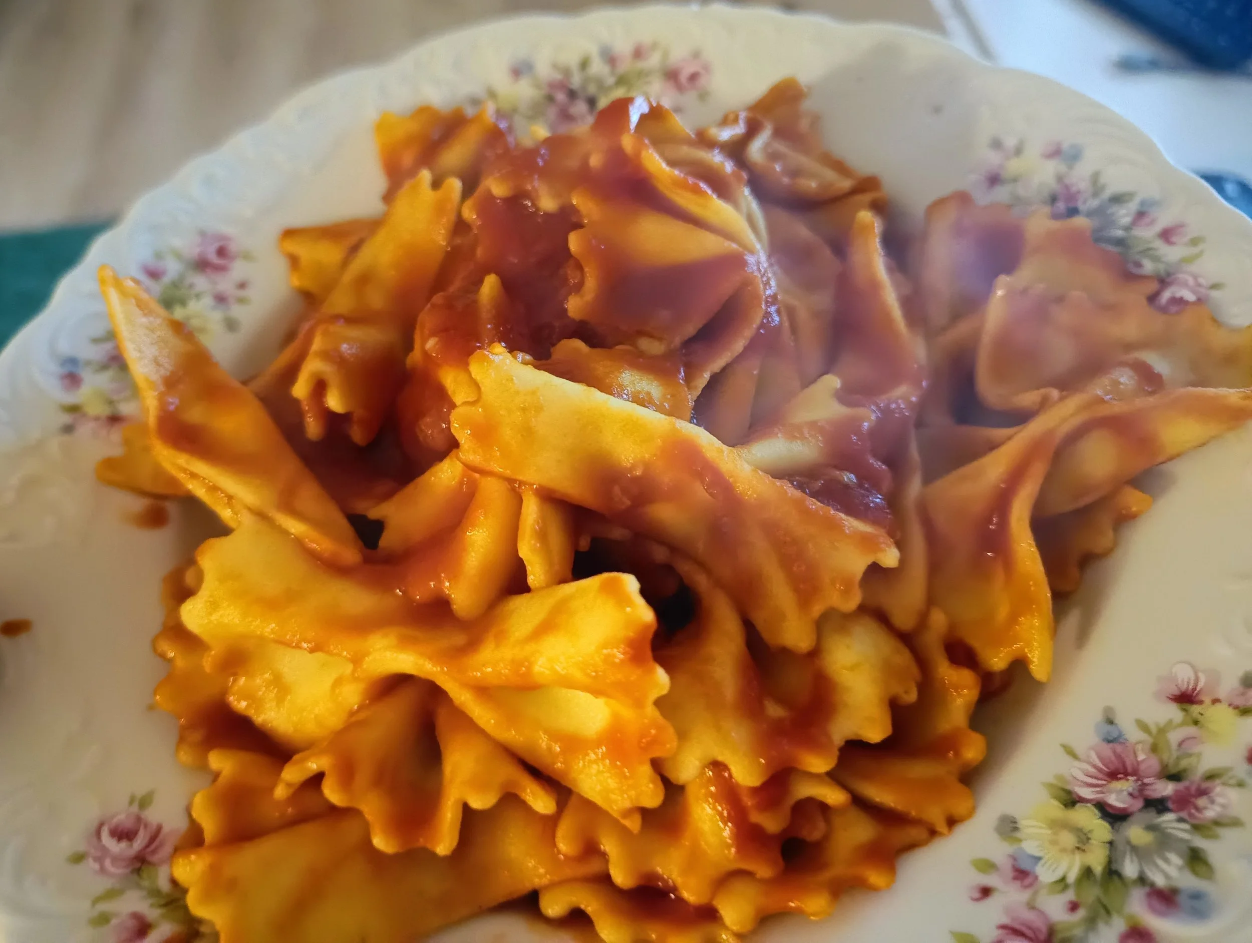 Fresh handmade farfalle served with tomato sauce on a floral plate.
