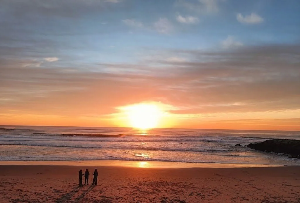 Three people standing close together at sunset, suggesting intimacy, connection, and diverse forms of relationship.