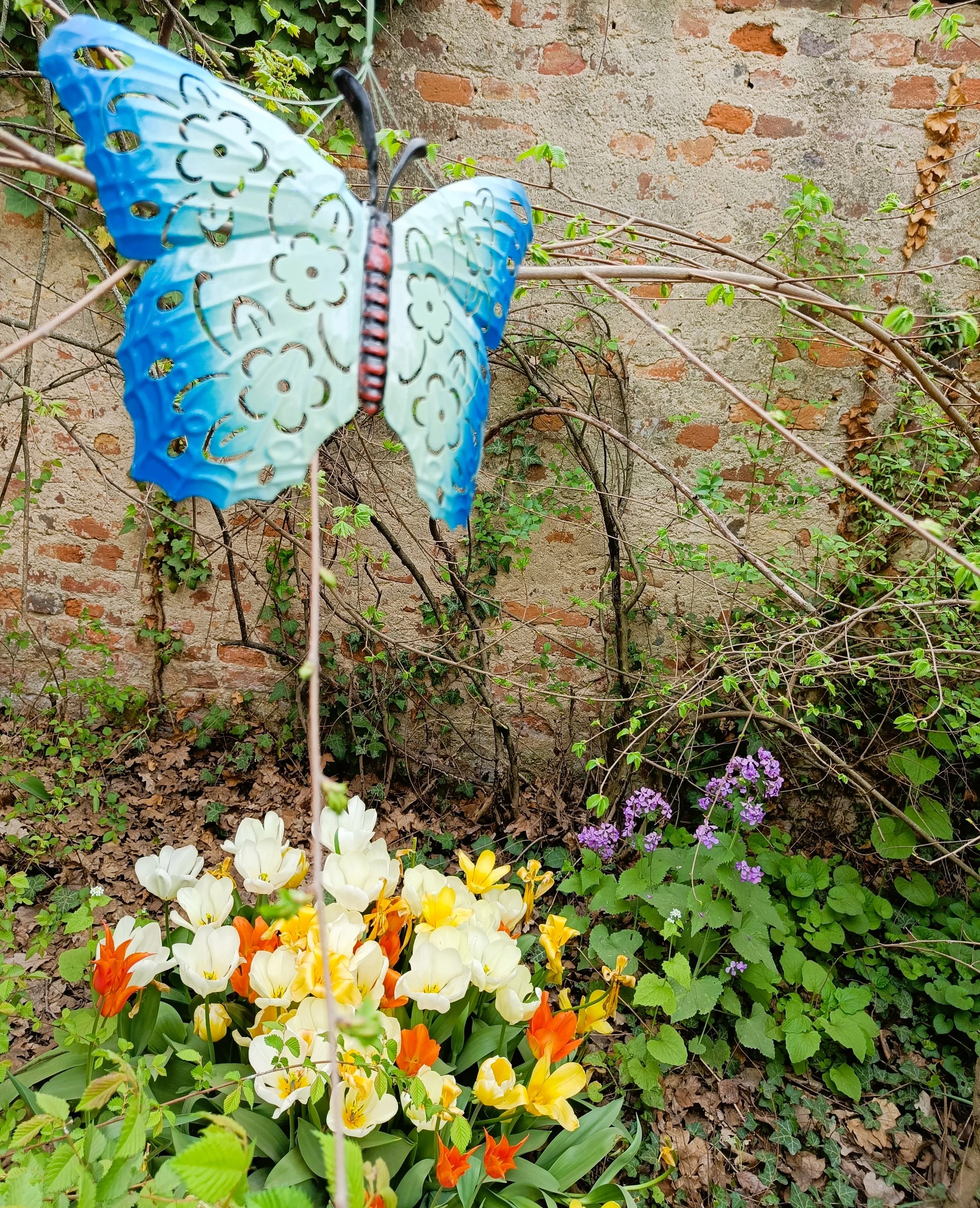 A decorative blue butterfly on a stick among flowers and greenery, suggesting stillness and suspension.