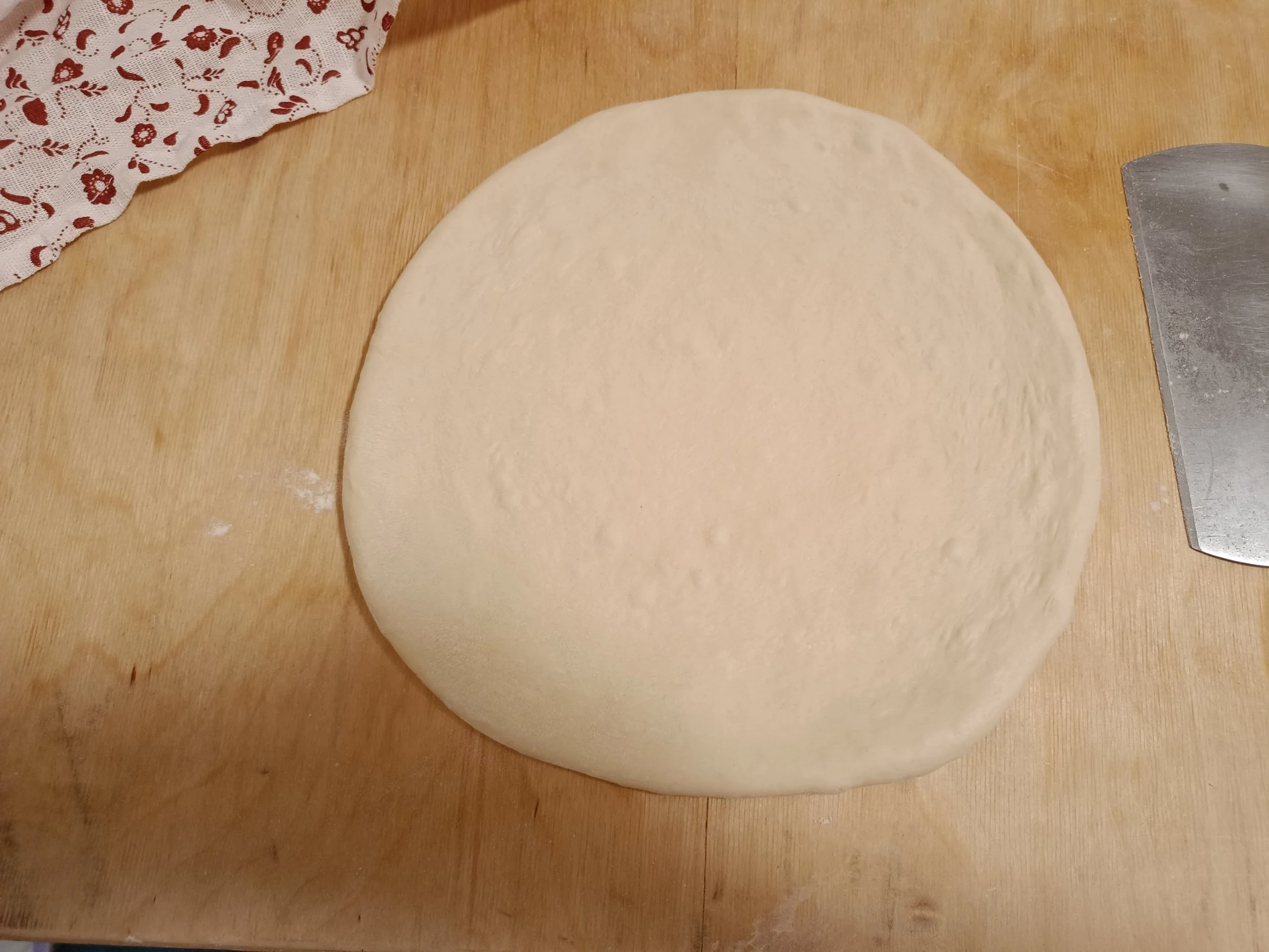 Stretched Neapolitan-style pizza dough on a wooden surface, ready for topping.