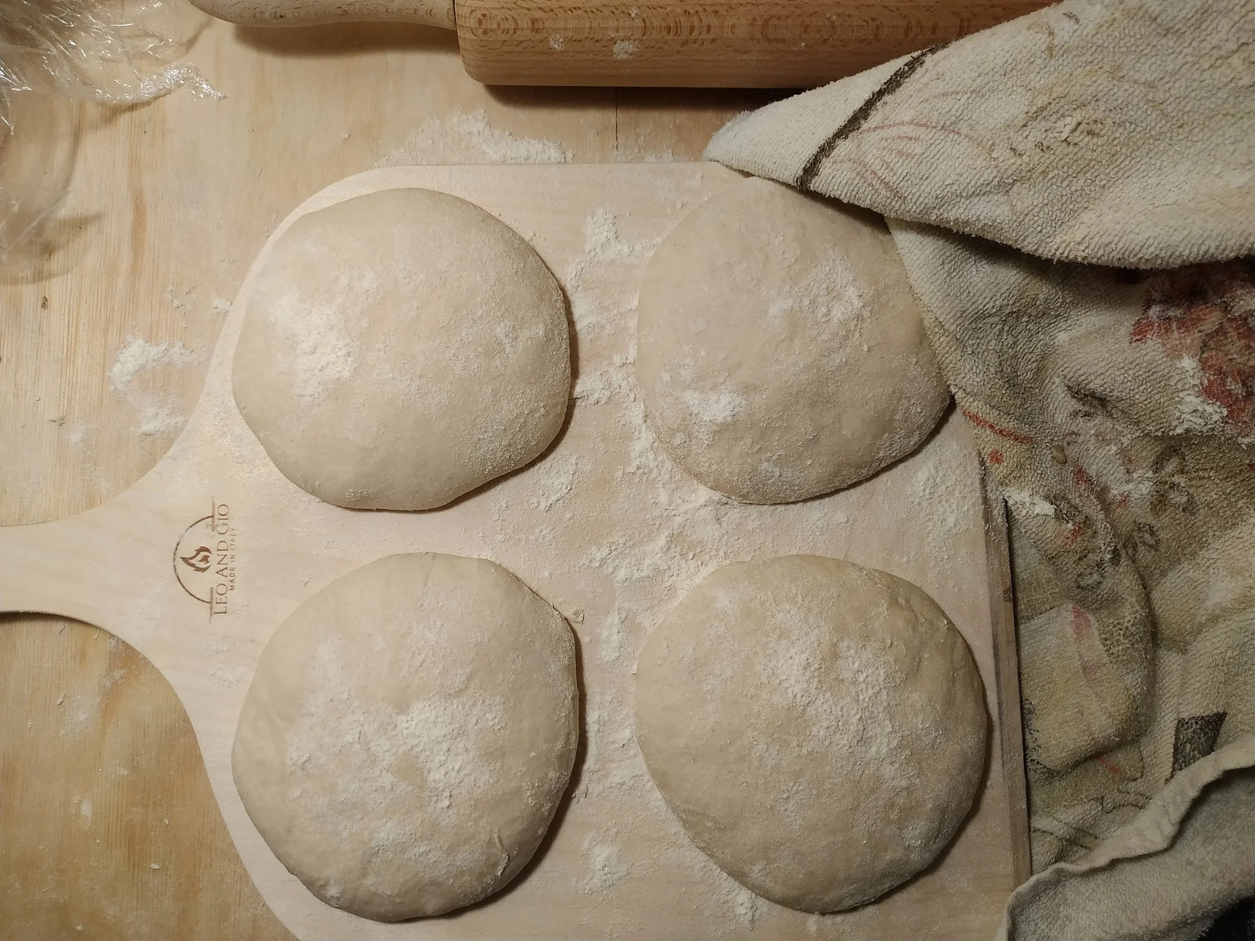 Homemade Neapolitan pizza dough balls resting on parchment paper on a wooden surface.