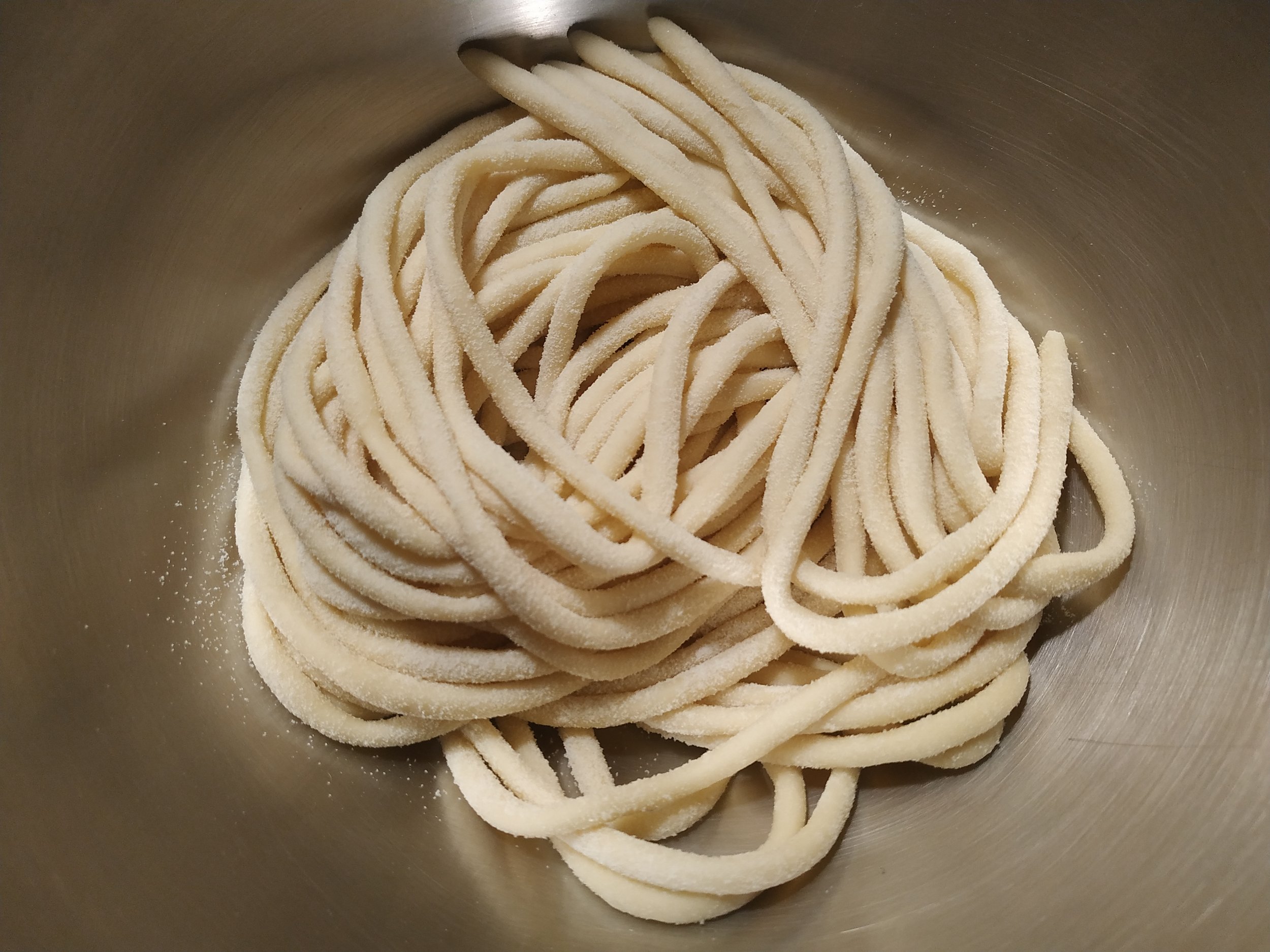 Fresh handmade tagliatelle in a stainless steel bowl.
