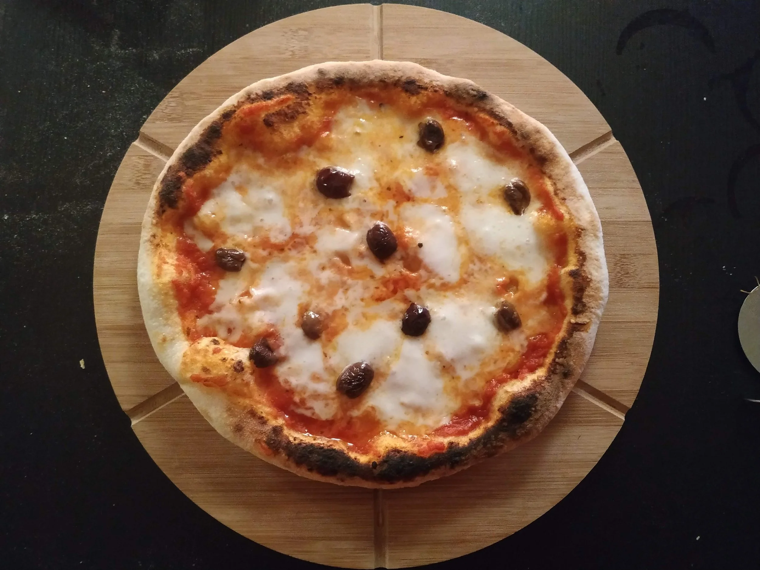A pepperoni pizza with melted cheese and a slightly charred crust on a wooden pizza board.