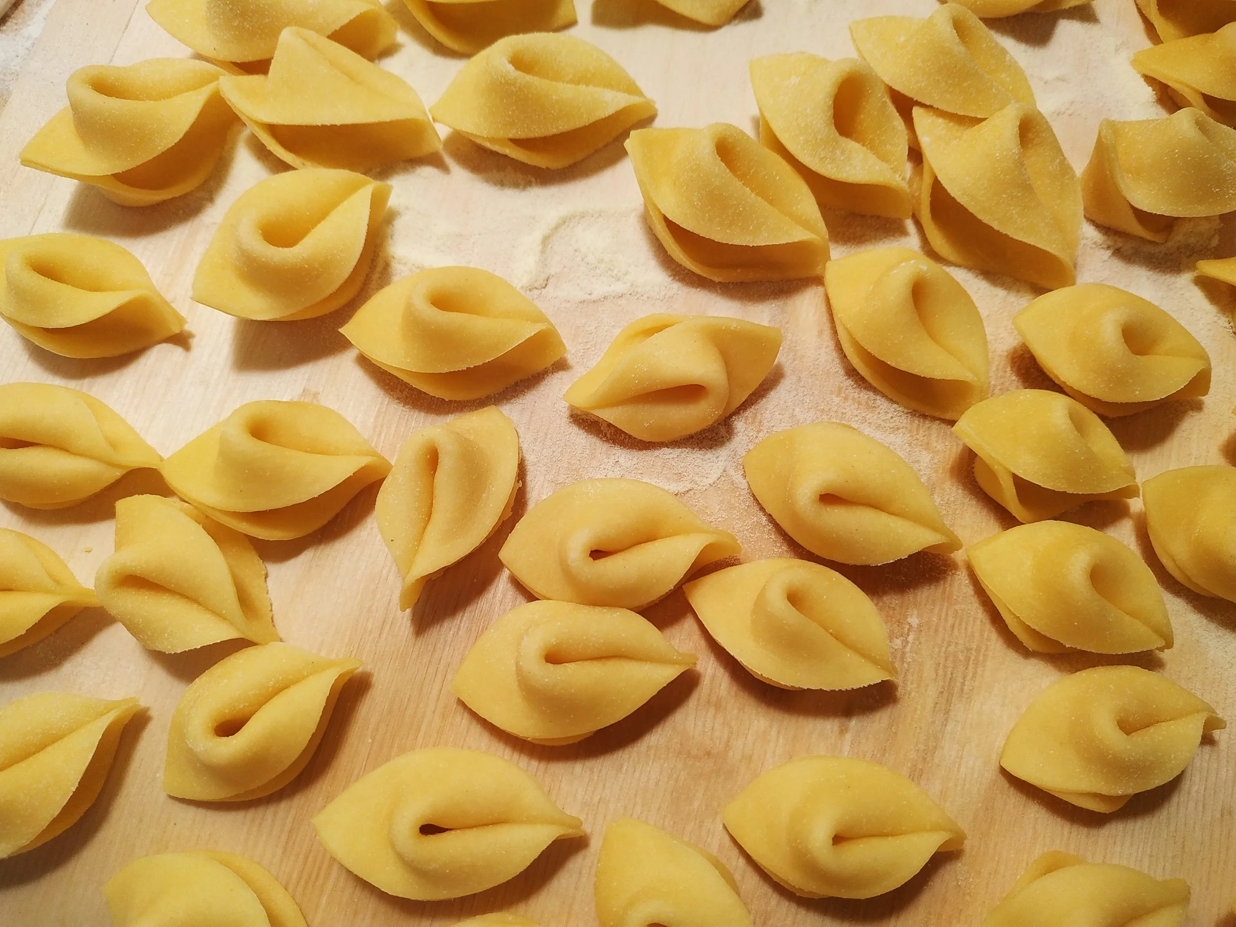 Fresh handmade cappelletti arranged on a wooden surface dusted with flour.