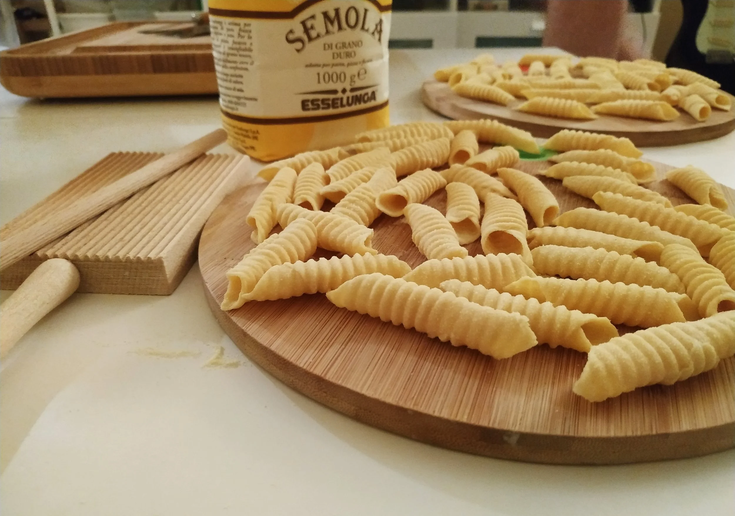 Fresh handmade shell-shaped pasta on a wooden board, with Semola di Grano Duro flour in the background.