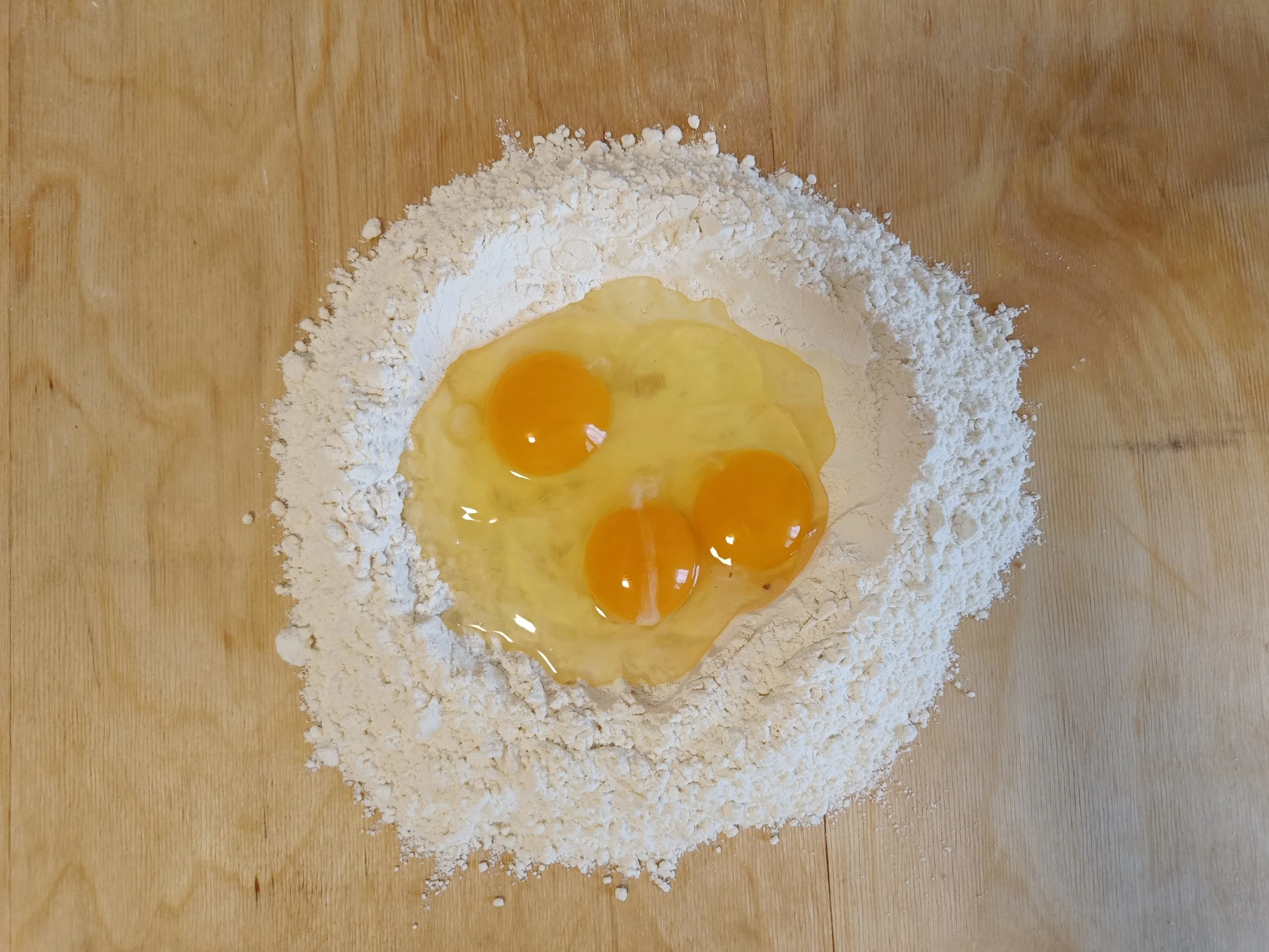 Flour and eggs arranged on a wooden surface, showing the first step in making fresh pasta dough.