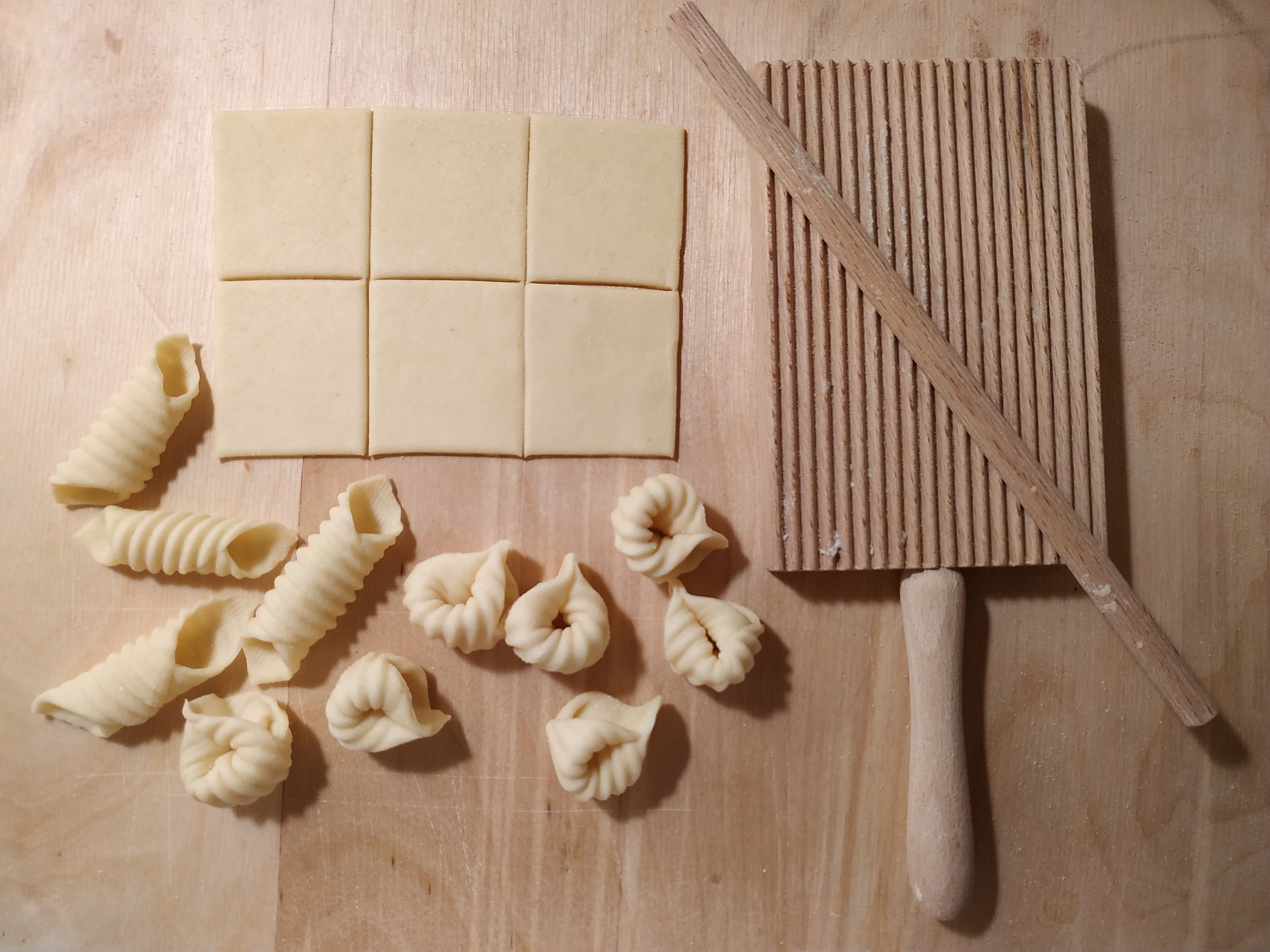 Handmade orecchiette-style fresh pasta shapes on a wooden surface.
