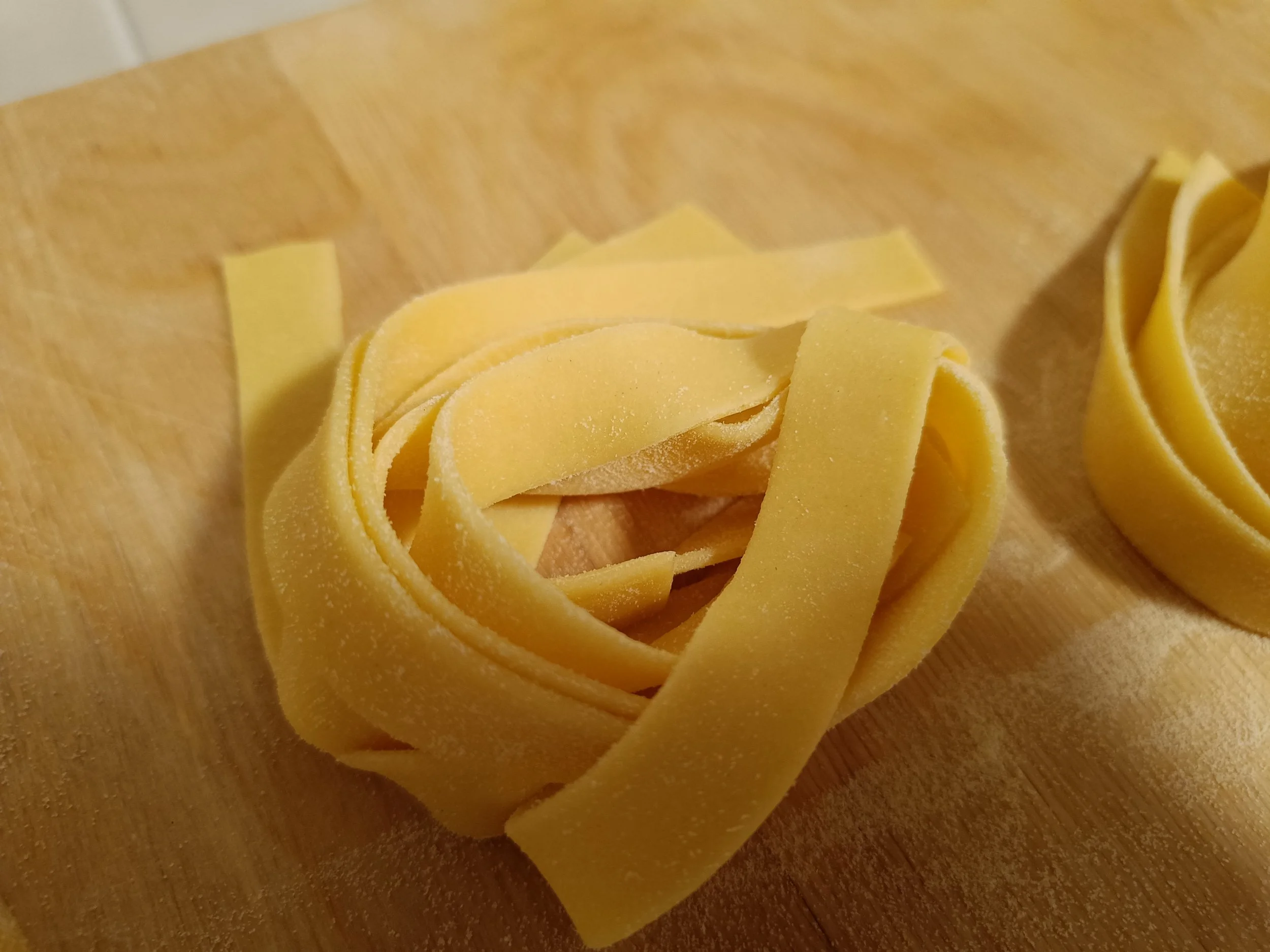 Fresh handmade fettuccine nests on a wooden surface.
