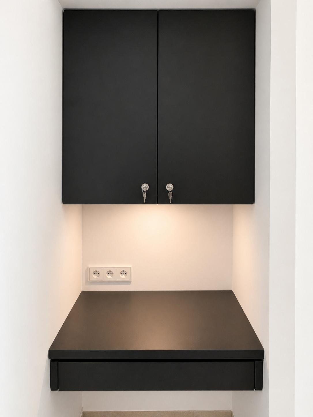 Meuble noir fixé au mur avec deux portes sécurisées par des cadenas, un bureau noir en dessous, et une prise électrique à trois fiches
