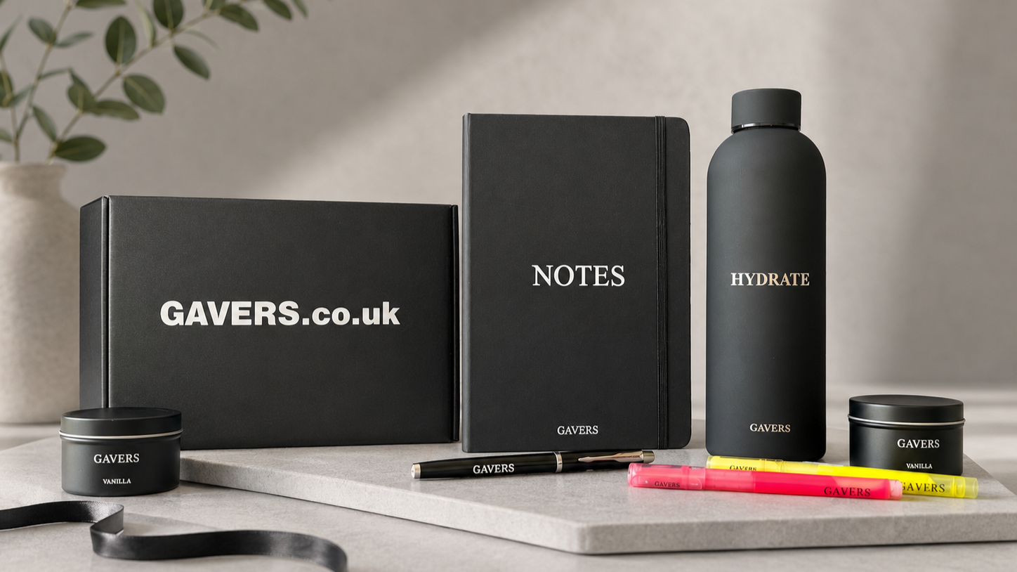 Gavers product collection including black box labeled Gavers.co.uk, black notebook labeled NOTES, black water bottle labeled HYDRATE, black tins labeled Gavers Vanilla, pink and yellow highlighters, and black pen, all arranged on a neutral background with a plant in a pot in the background.