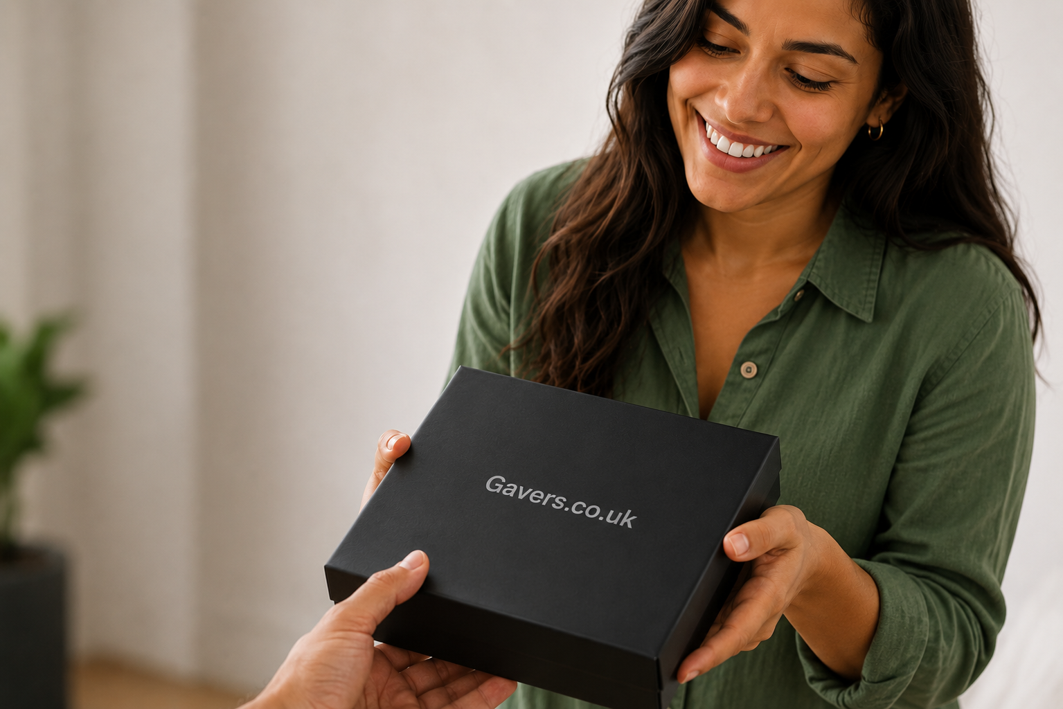 A woman in a green shirt receives a black box with the website Gavers.co.uk printed on it, smiling as she looks at the box.