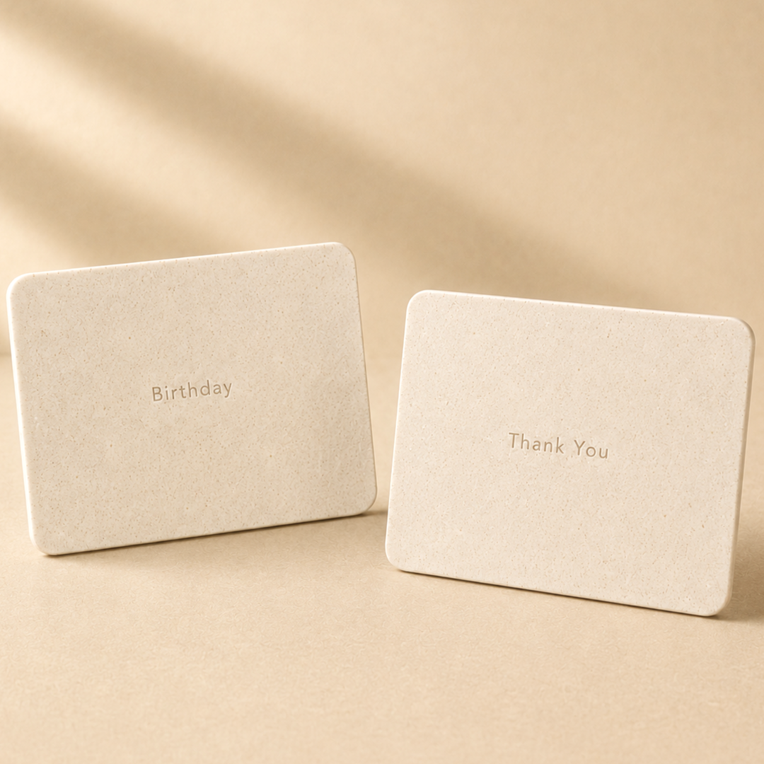 Two beige Gavers greeting cards, one with 'Birthday' and the other with 'Thank You' written on them, placed on a matching beige surface with a softly lit background.