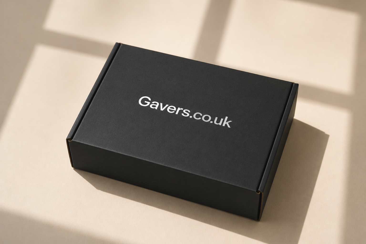 Black packaging box with white text that reads Gavers.co.uk, placed on a beige surface with shadow patterns.