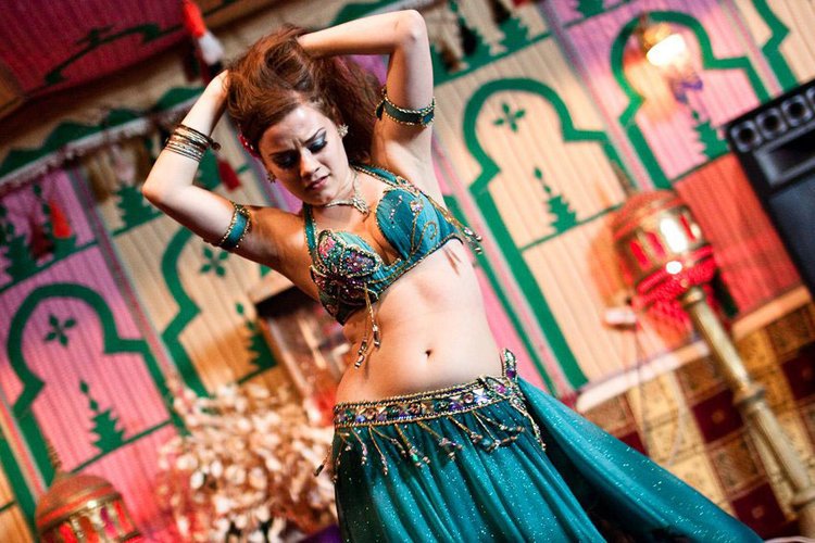 A woman dressed in a blue belly dance costume performing in a colorful decorated room.