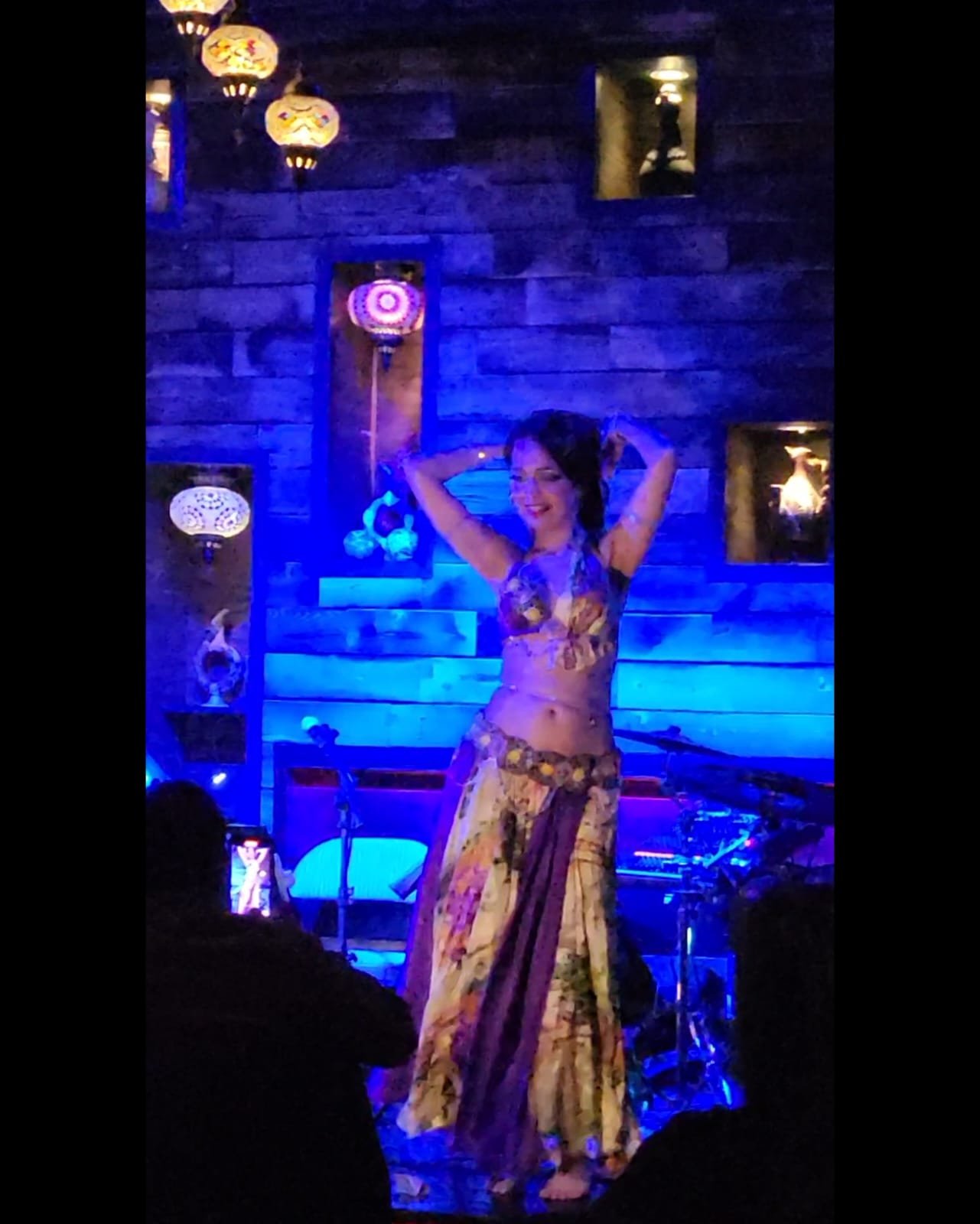 A woman in a floral dress performing on a stage decorated with Asian-style paper lanterns and wood paneling, lit with blue lighting.