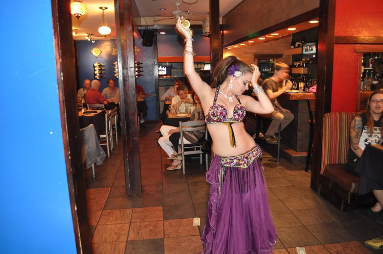 A belly dancer performing in a restaurant interior with seated diners watching.