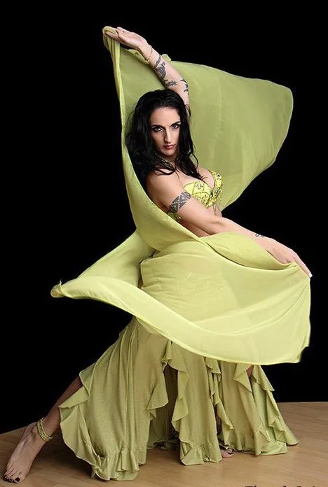 A woman in a yellow dress posing with flowing fabric against a black background.