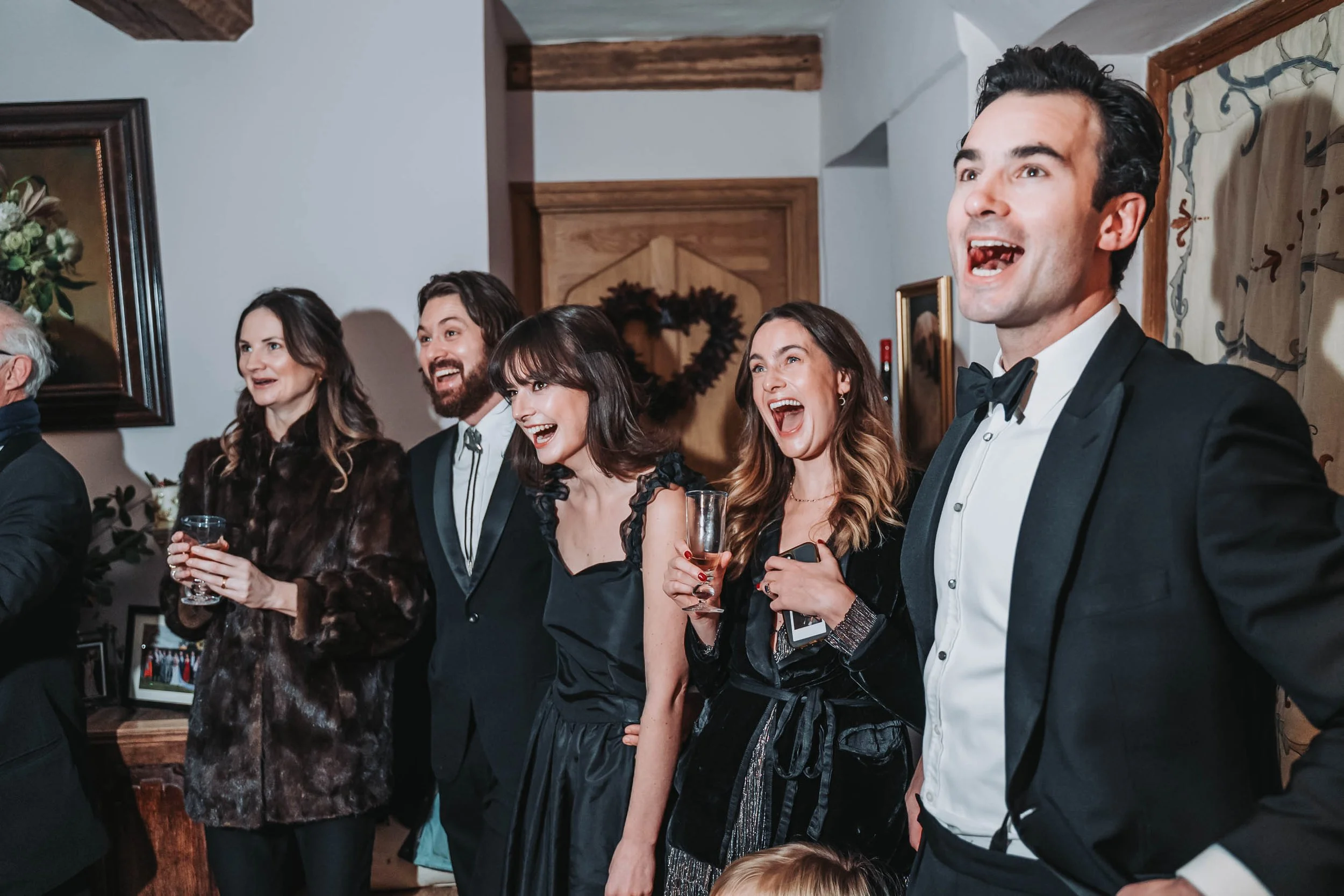 Group of people dressed in formal attire at a celebration, smiling and holding glasses, indoors.