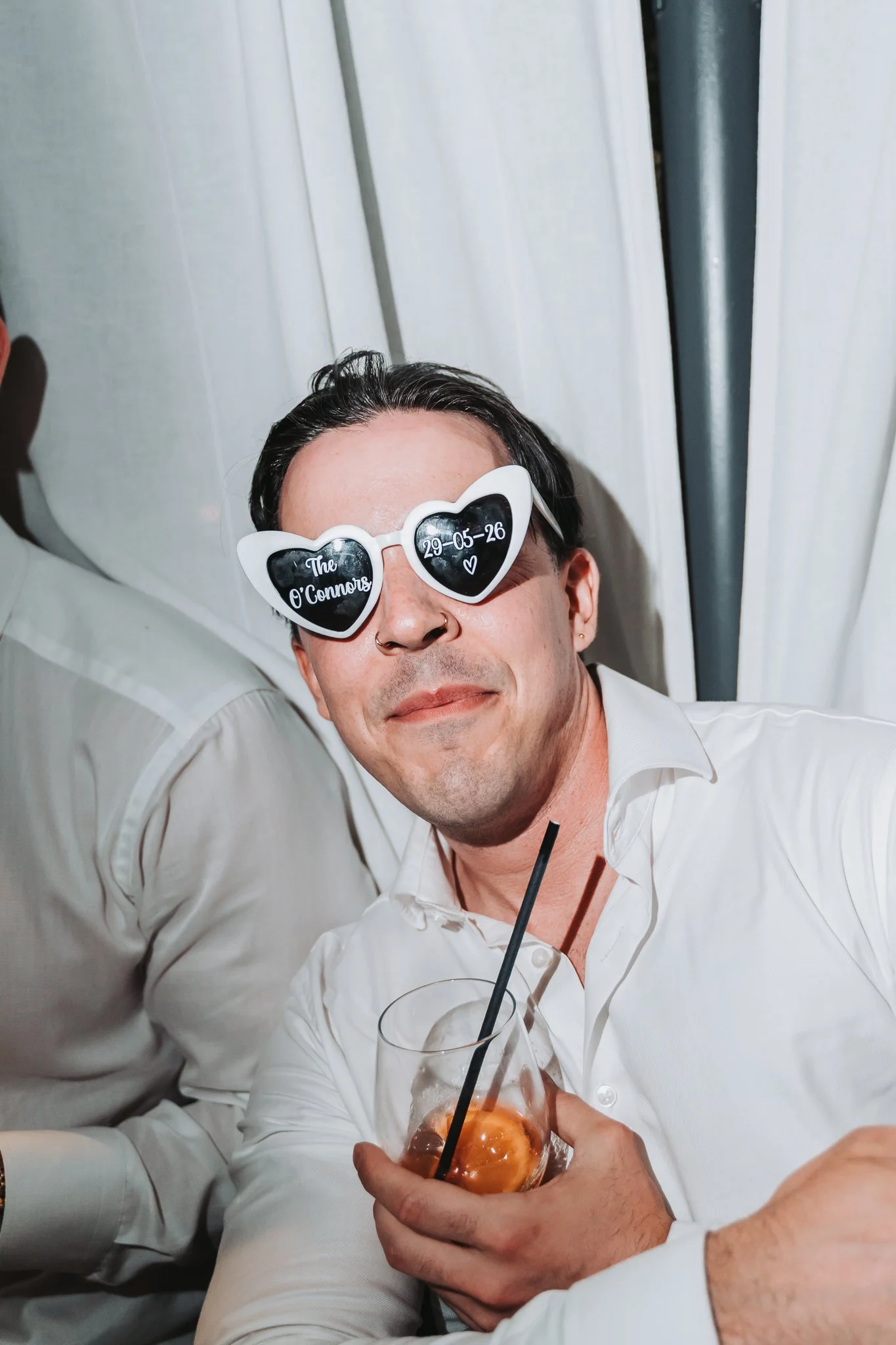 A man wearing heart-shaped sunglasses with the words 'The O'Connors' and a date, smiling while holding a glass of ice cream topped with caramel.