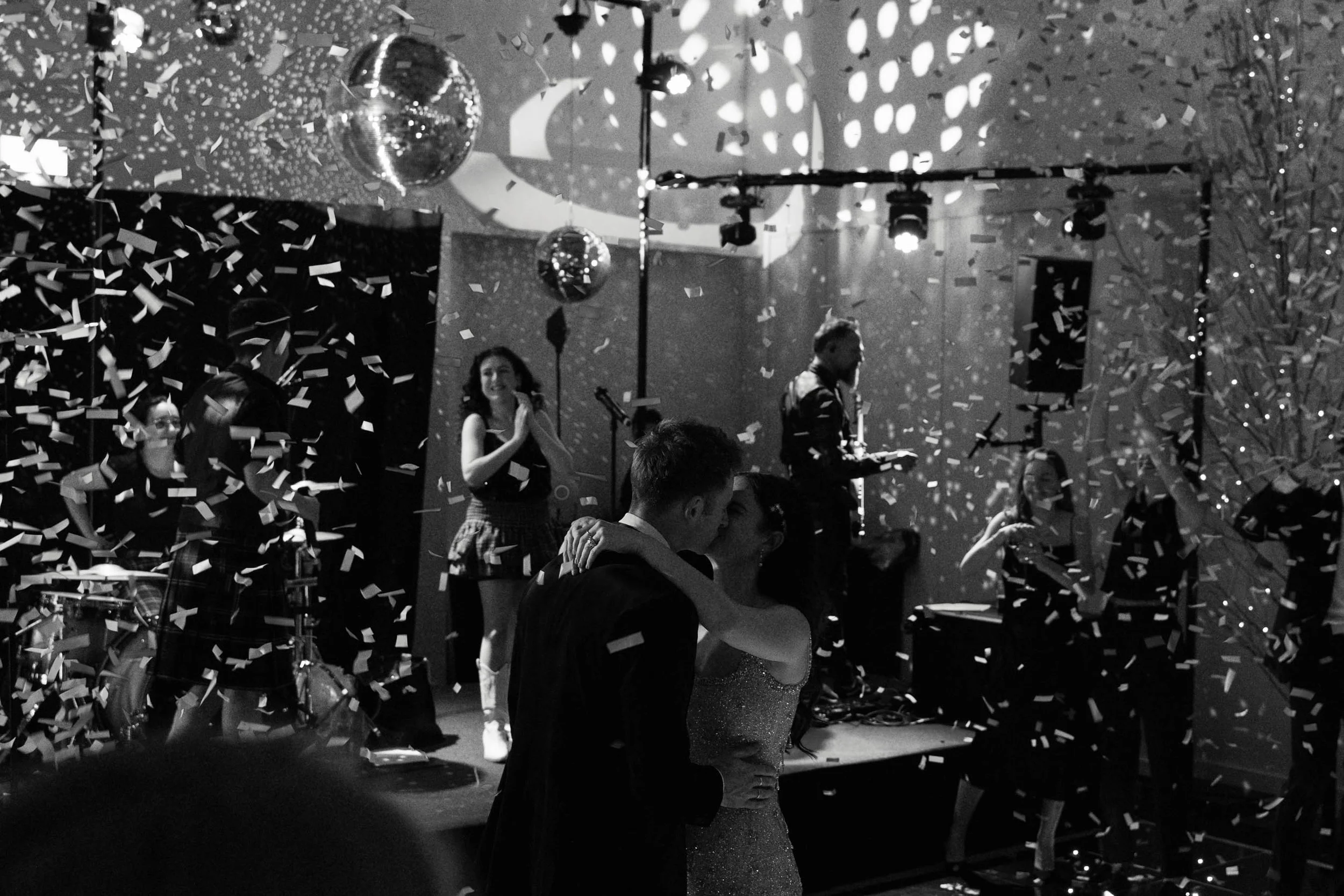 People dancing and celebrating at a party with confetti, disco balls, and stage lighting.