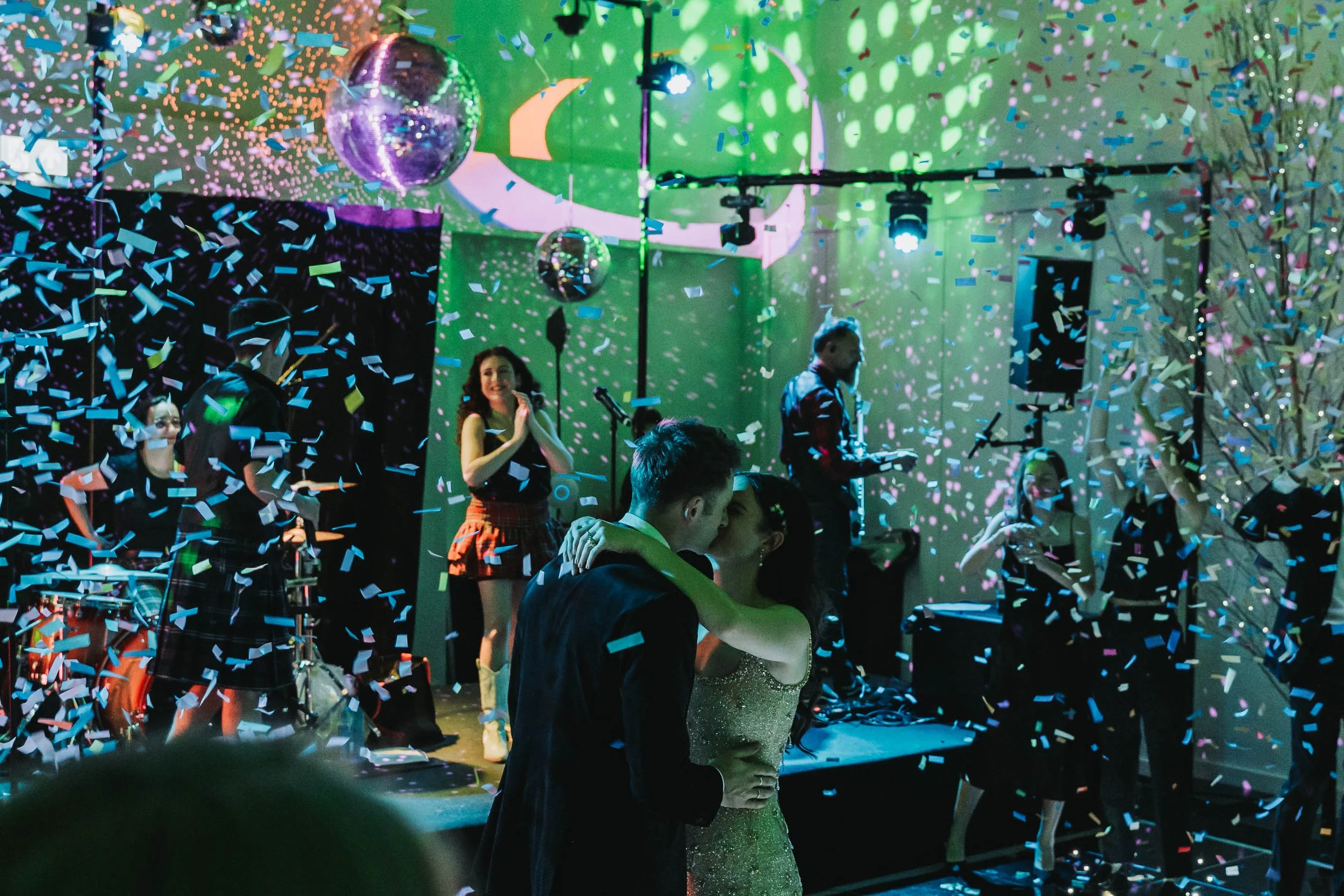People dancing and celebrating at a party with confetti, disco balls, and colorful lights.