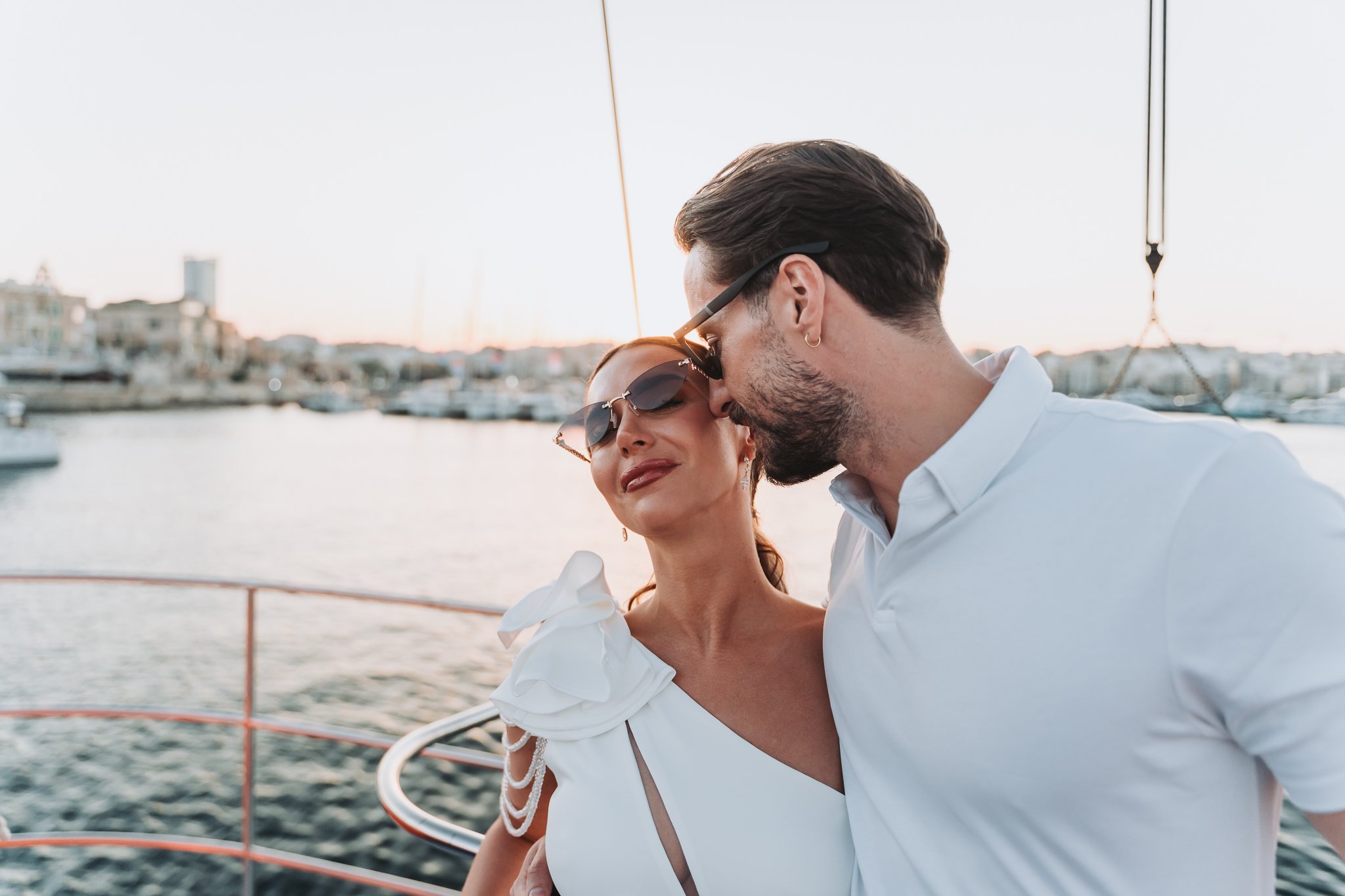 A couple embracing on a boat with water and marina in the background during sunset.
