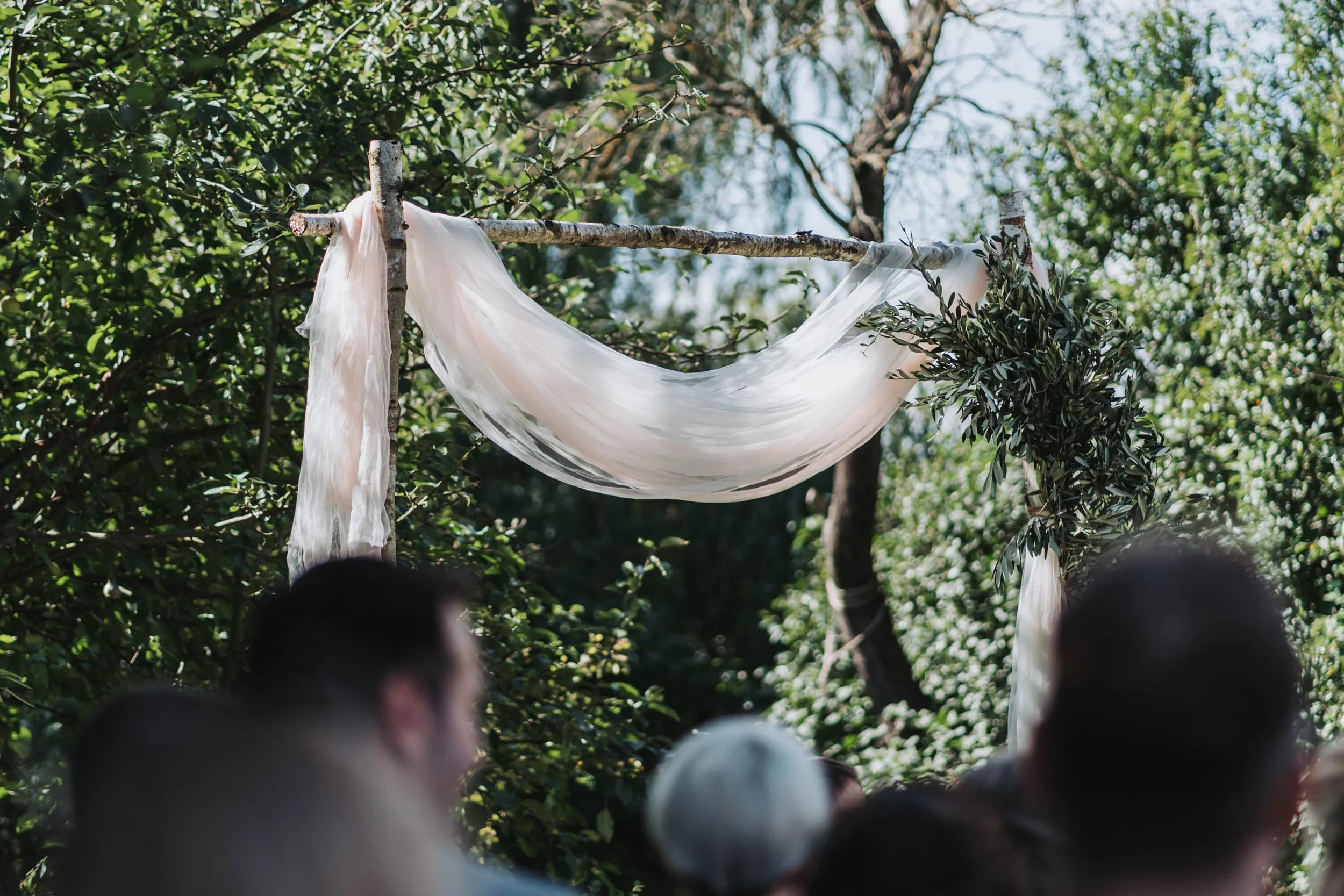 A white fabric draped over a wooden branch against a backdrop of green foliage and trees.