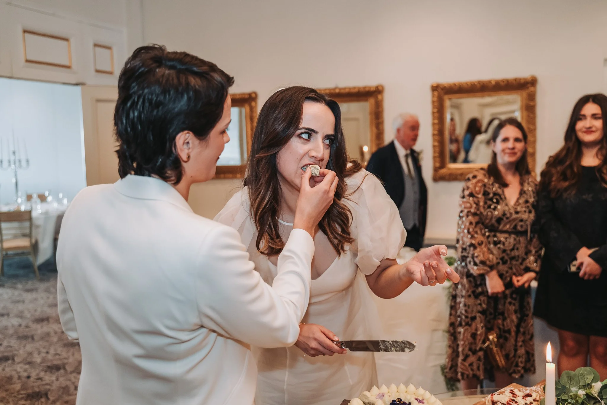 Women at a celebration table, some women are in the background, one woman is serving cake, others are smiling.