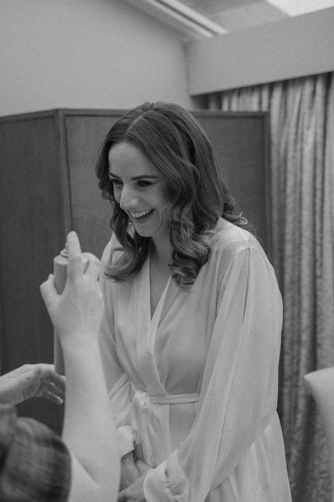 Black and white photo of a woman smiling and looking down as someone hands her a small, wrapped gift.