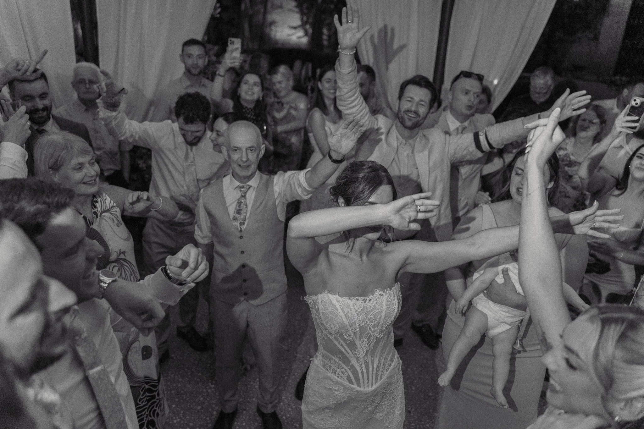 A group of people at a party dancing and celebrating, some taking pictures and waving their hands in the air.