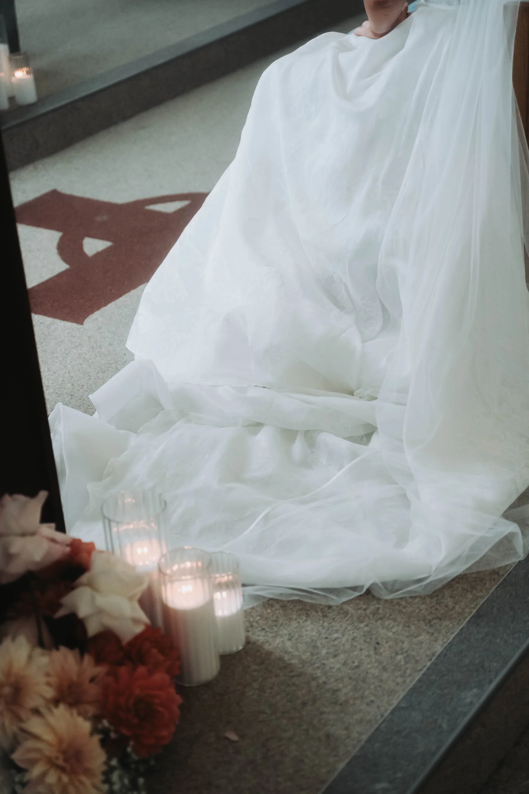 Close-up of lit white candles and a floral arrangement with pink and cream flowers placed on a table or altar surface.