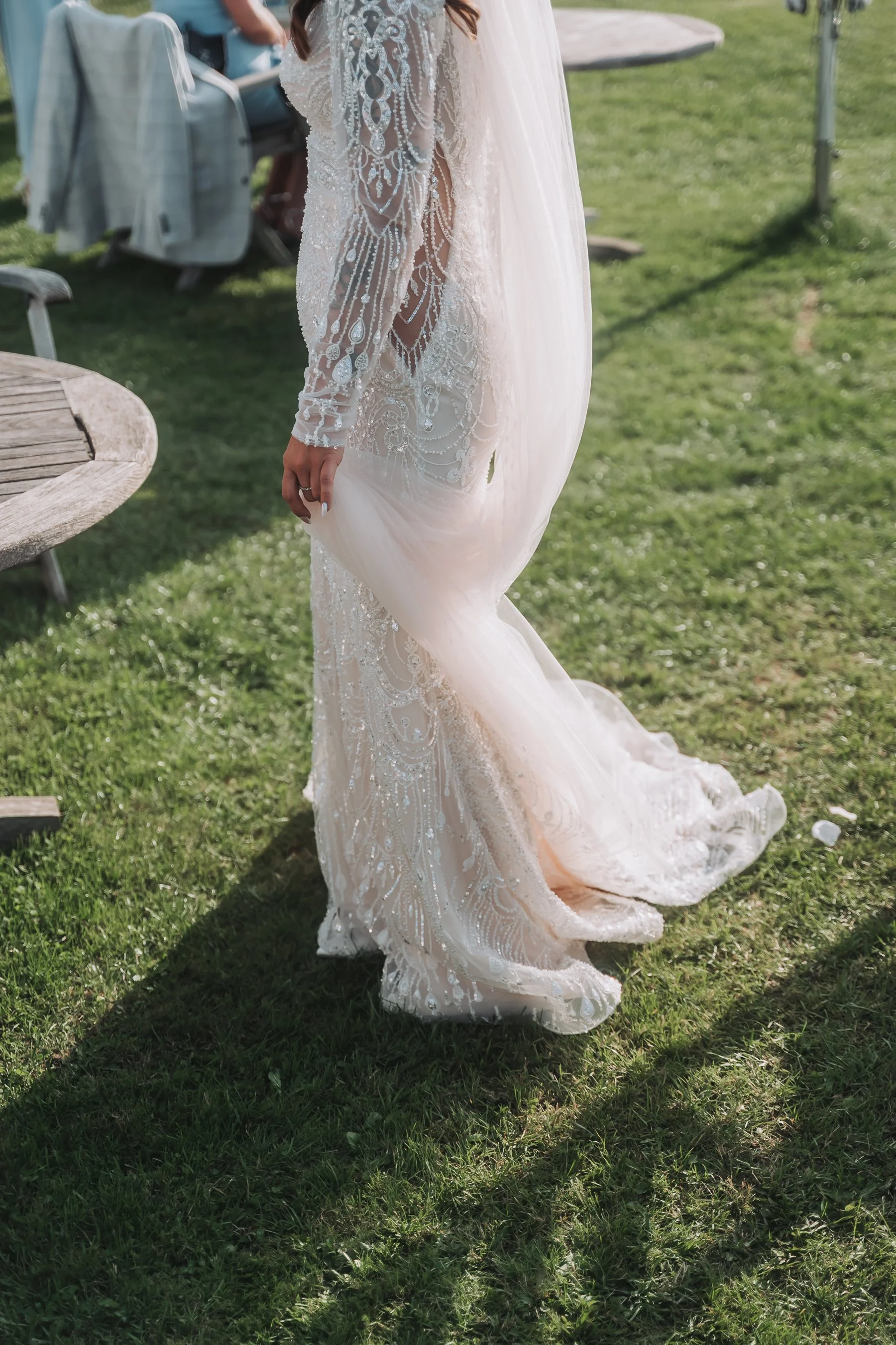 A person wearing a detailed, white lace wedding dress standing on grass at an outdoor event.