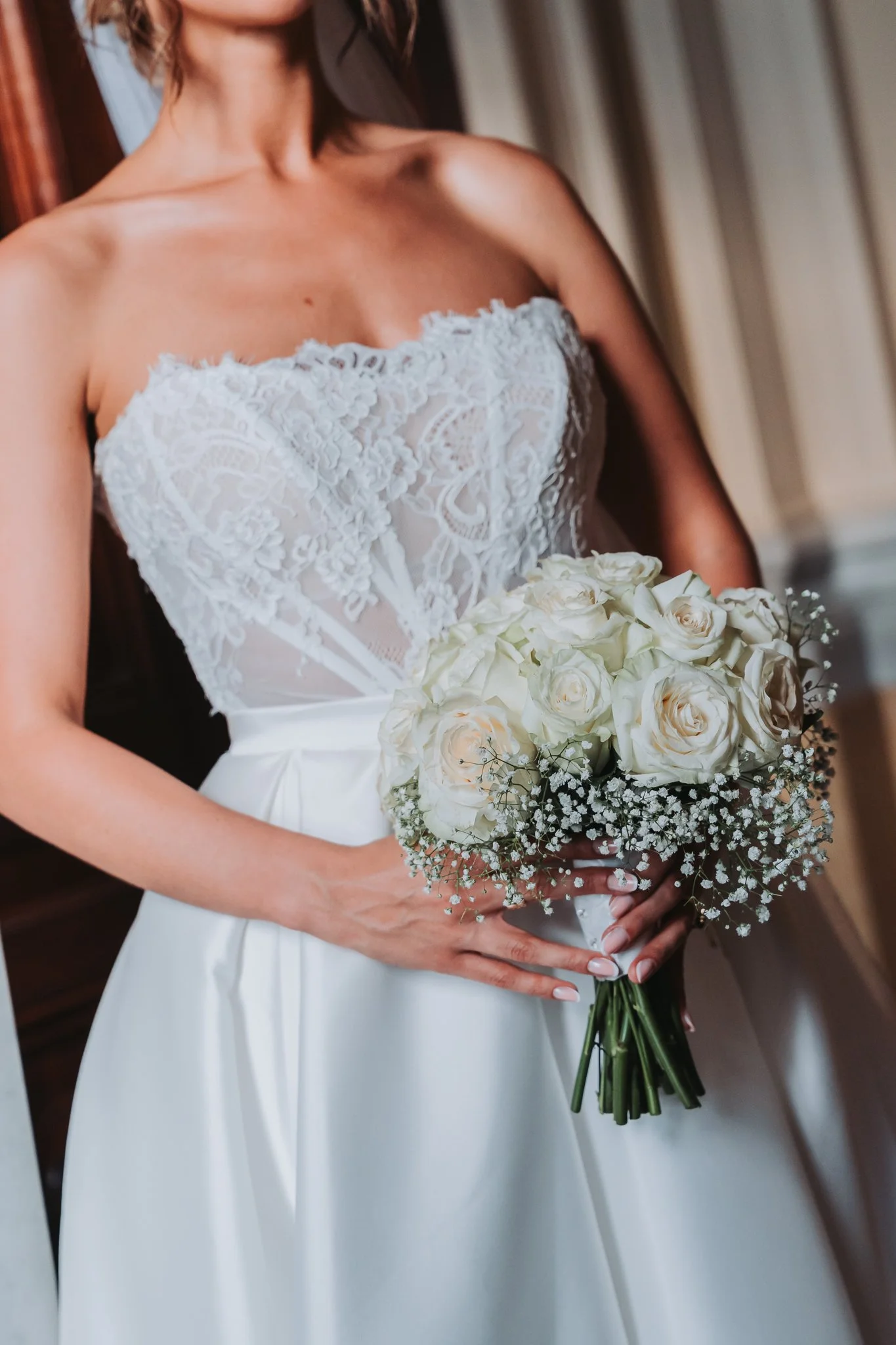 A bride wearing a white lace wedding dress holding a bouquet of white roses and baby's breath.