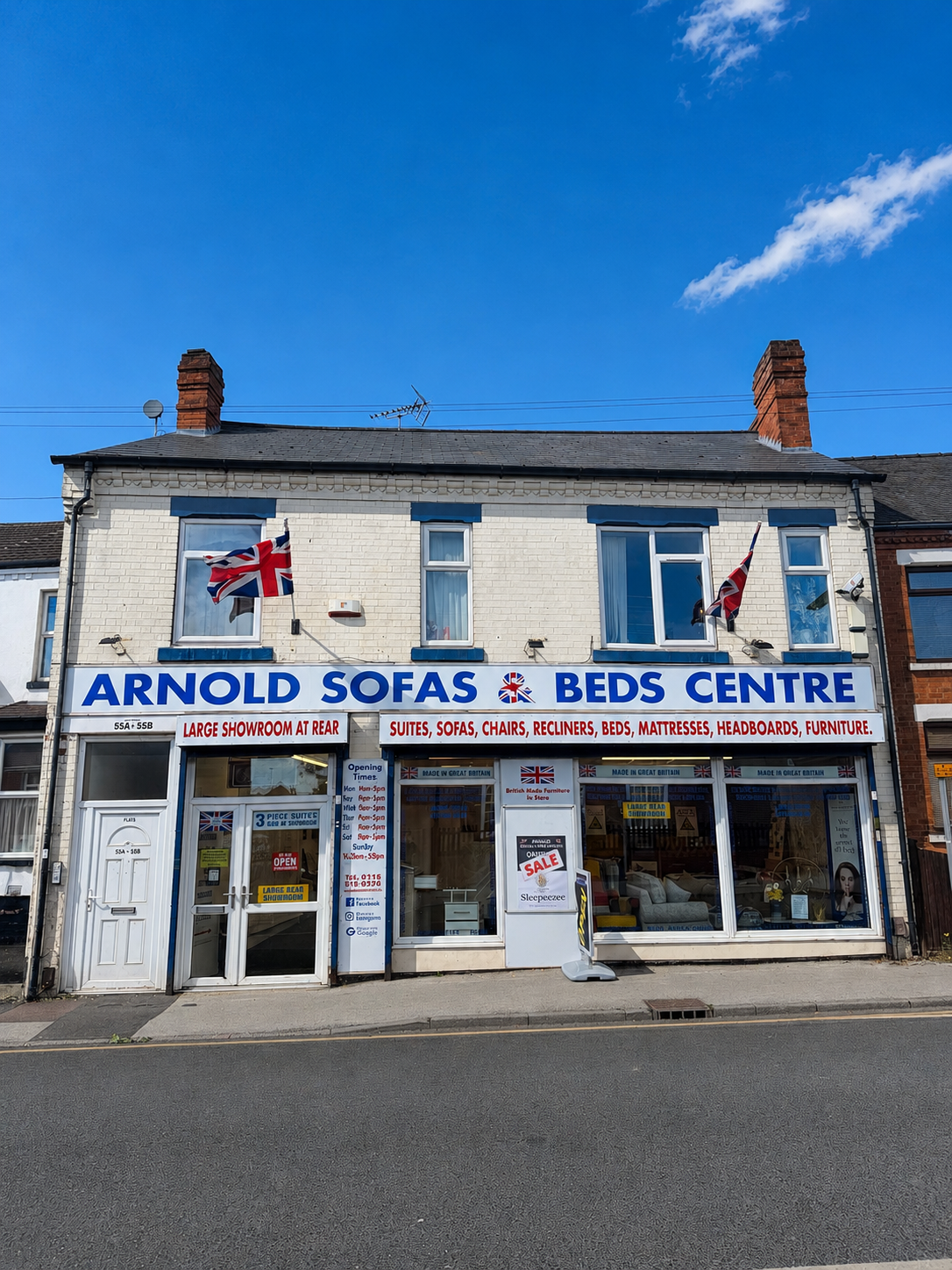 Front view of a furniture store called Arnold Sofas and Beds Centre with Union Jack flags, large signage, and windows displaying furniture inside under a clear blue sky.