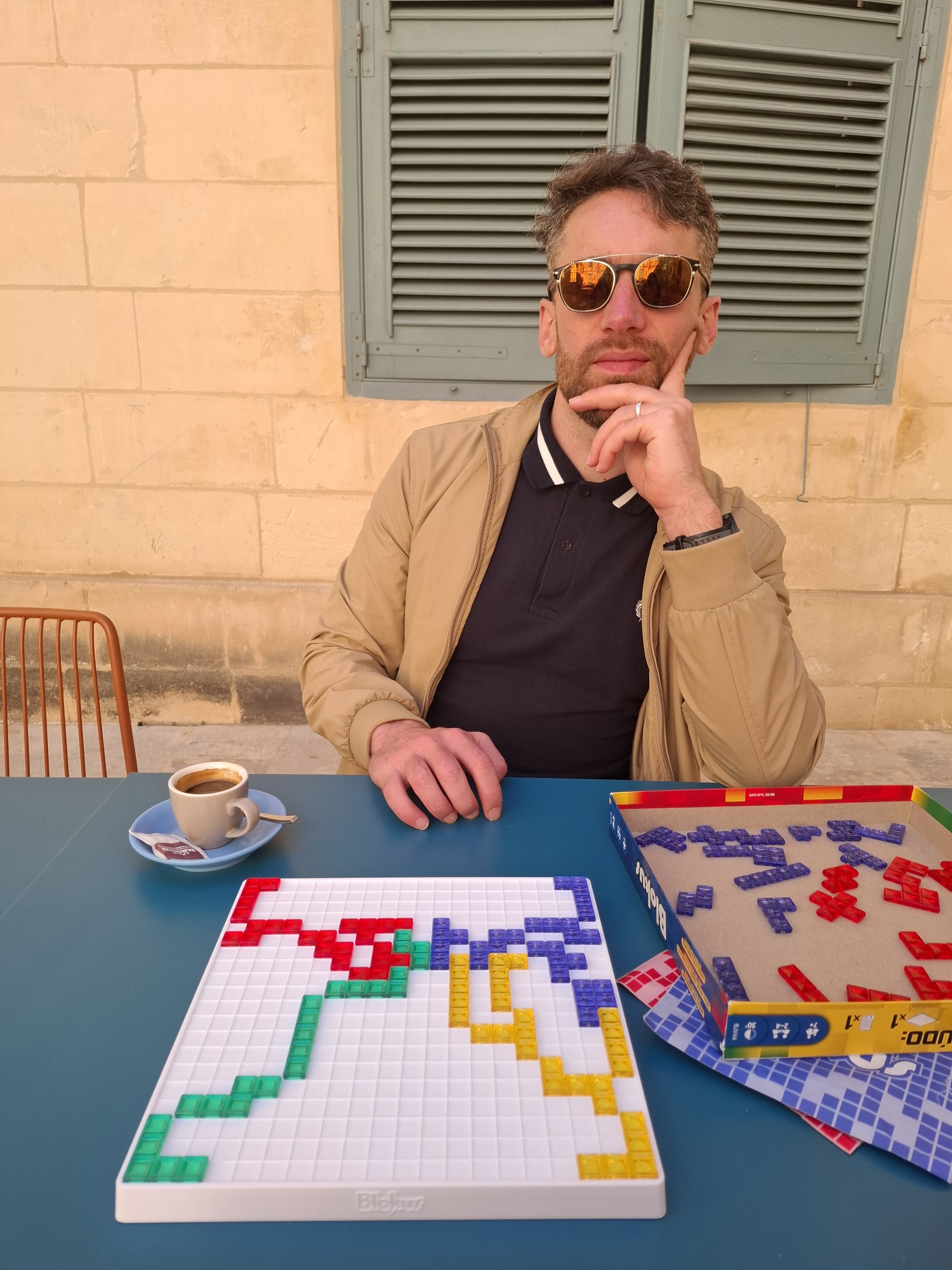 Young man in shades with a coffee and a board game.