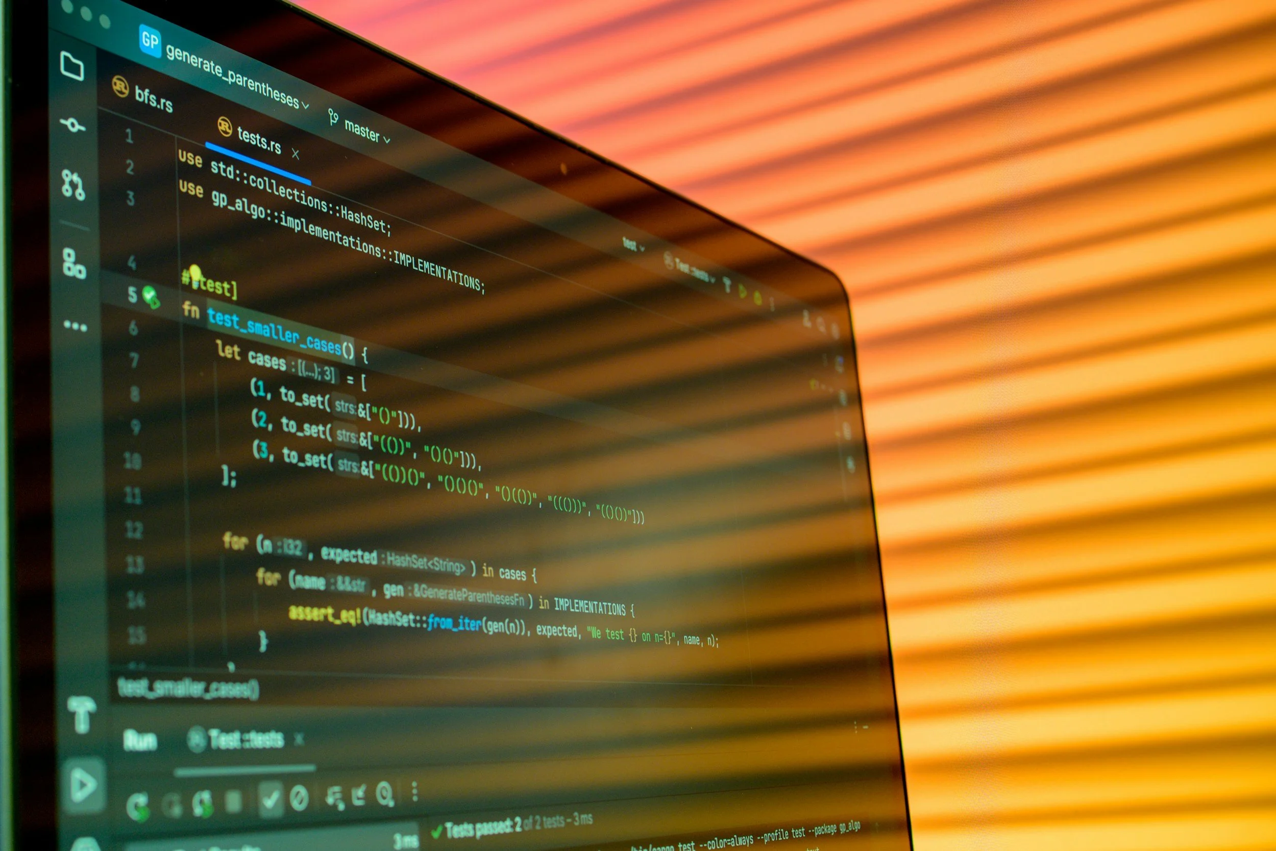 Close-up of a computer screen displaying code in a dark-themed code editor, with a blurred, warm-colored striped background.
