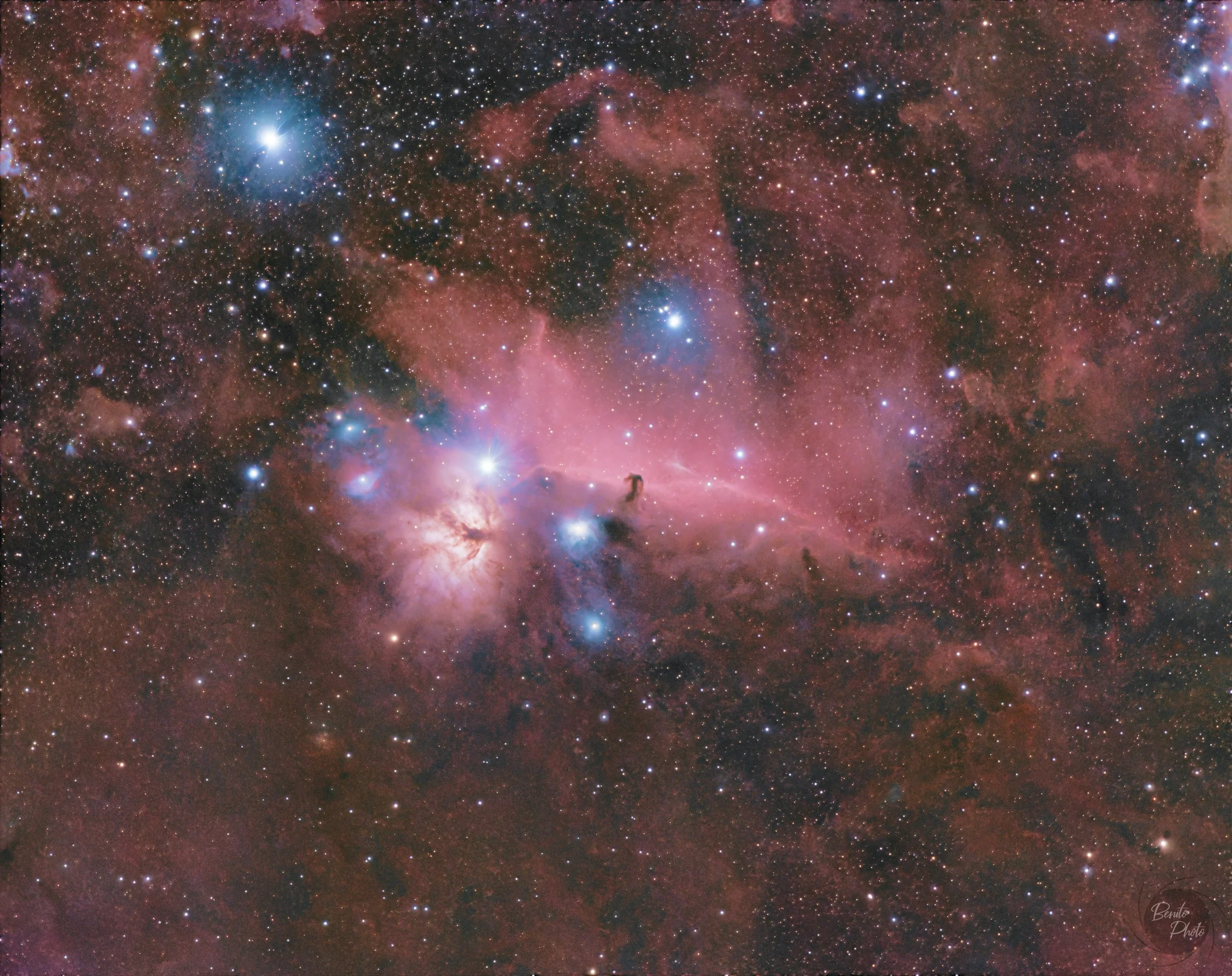 Une image d'une zone de l'espace avec de nombreux étoiles, une nébuleuse rougeâtre et des nuages de gaz et de poussière cosmique.