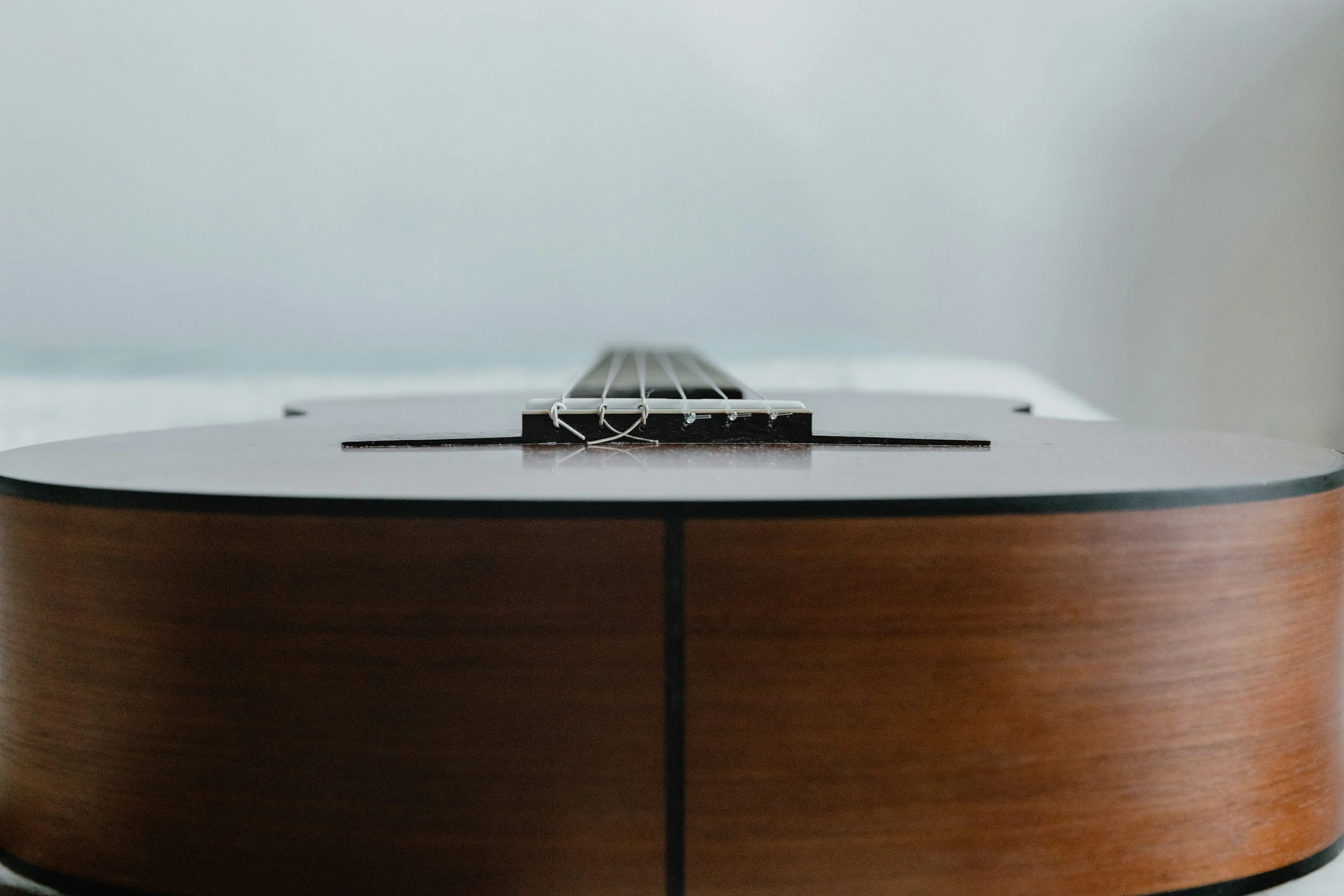 Close-up of the bridge of an acoustic guitar resting on a wooden table.