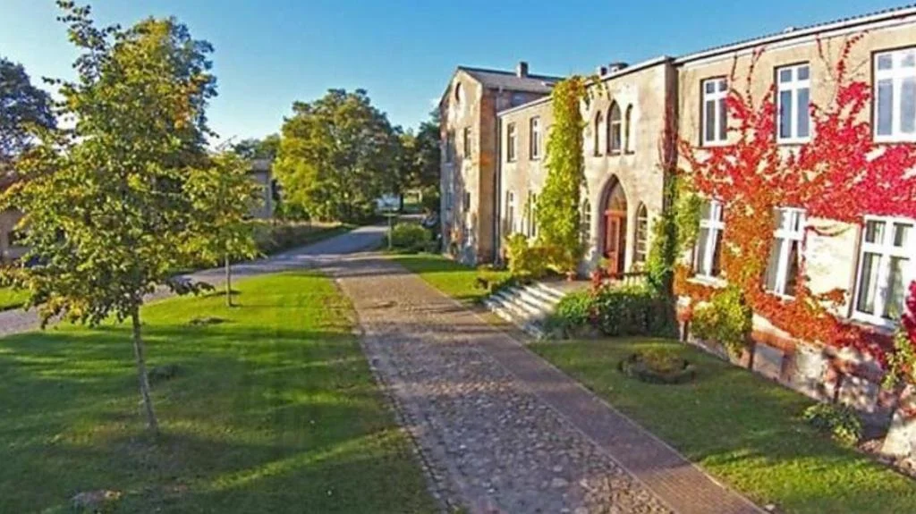 Ein ruhiger Weg, der an einer historischen Steinvilla mit roten und grünen Weinranken entlangführt, umgeben von gepflegtem Gras und Bäumen im sonnigen Park.