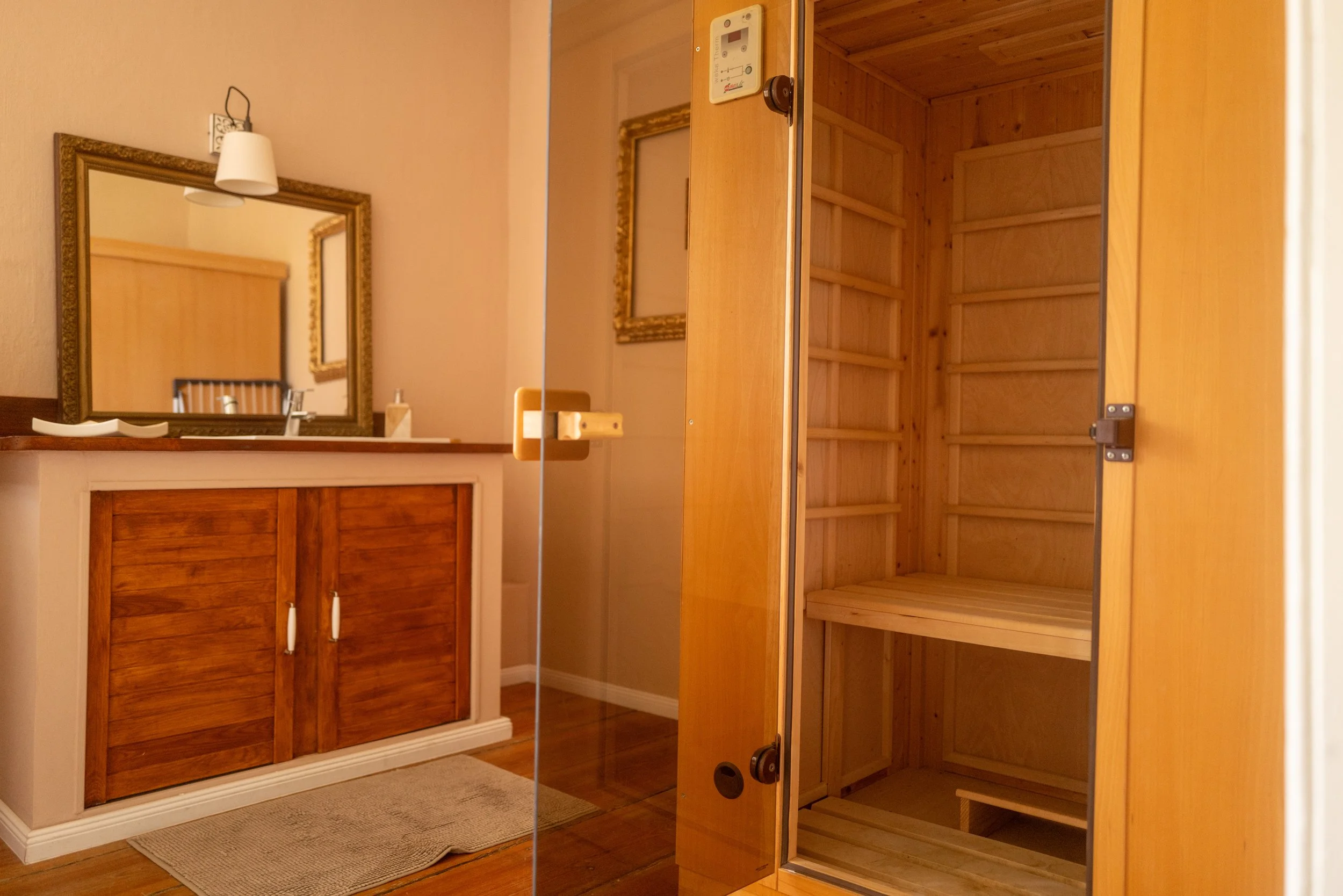 Ein leeres Holzregal in einem Raum mit Holzfußboden und Spiegel, neben einem Holzschrank mit doppelten Schiebetüren und einer Spiegelwand.
