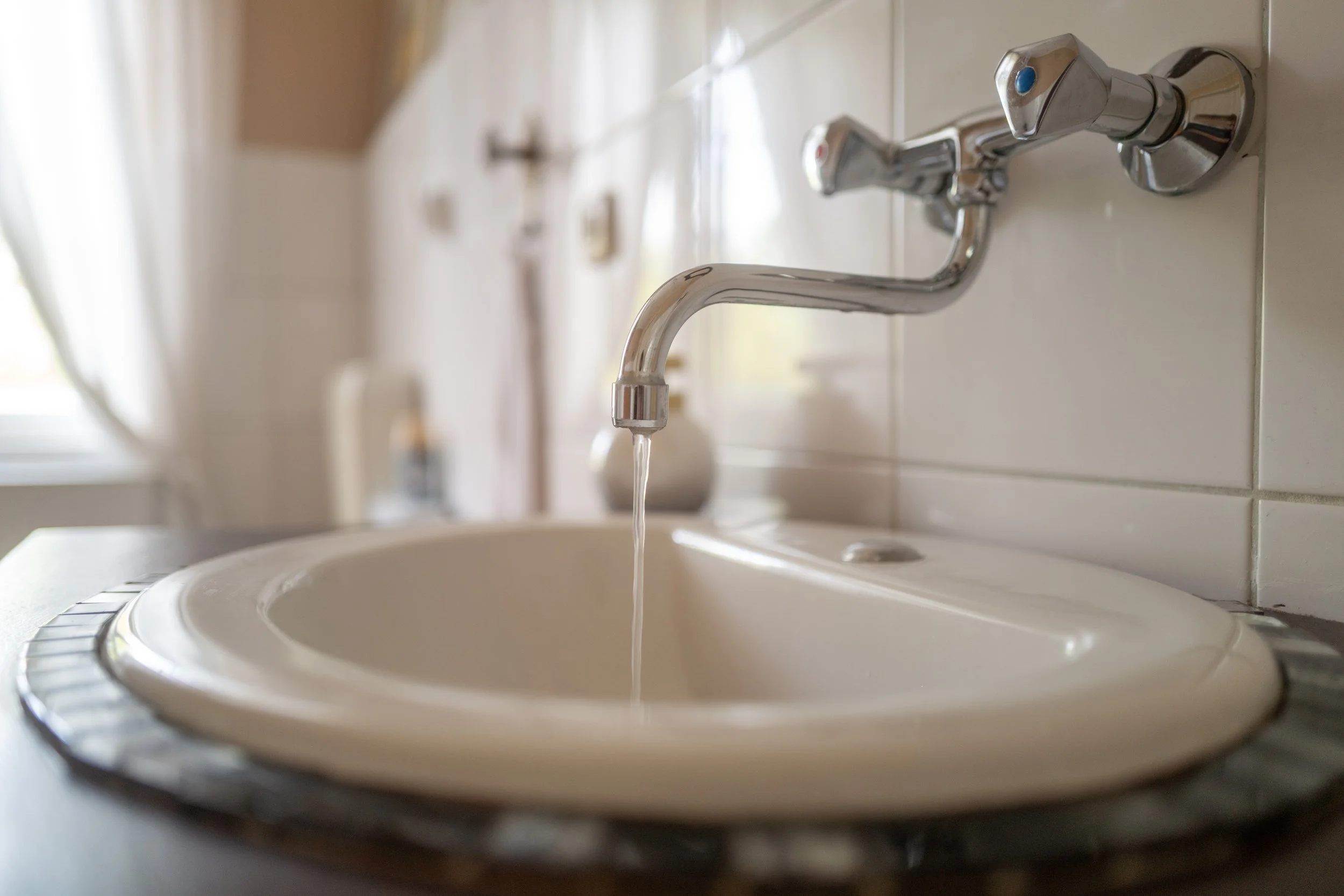 Ein Waschbecken mit Wasserhahn, Wasser läuft in das Becken, in einer modernen, hellen Umgebung.