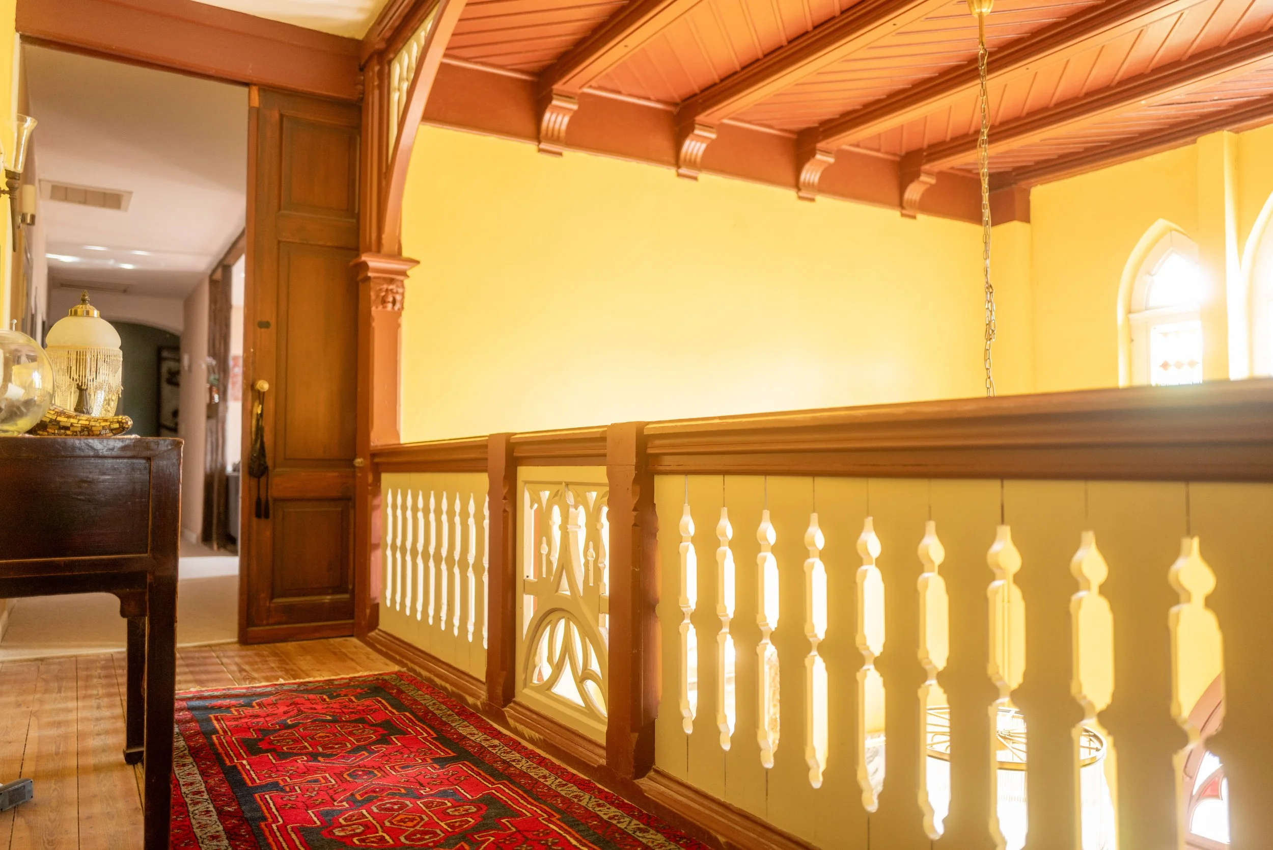 Innenansicht eines Hauses mit einem Balkon, Holzdecke, weißen Geländer, gelber Wand und Teppich auf dem Boden