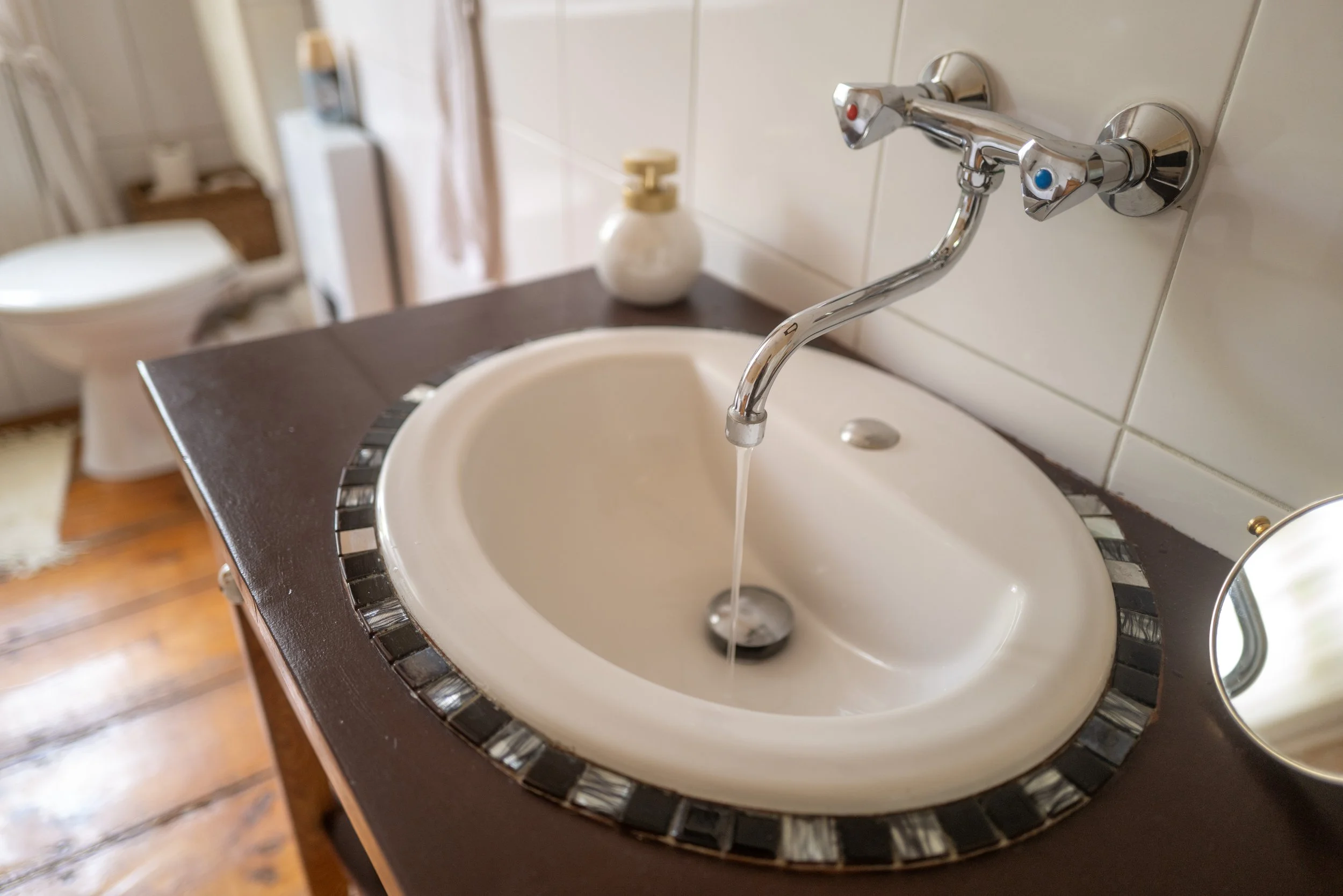 Ein Waschbecken mit Wasser, einem Wasserhahn mit zwei Griffen, einem Seifenspender im Hintergrund, im Badezimmer.