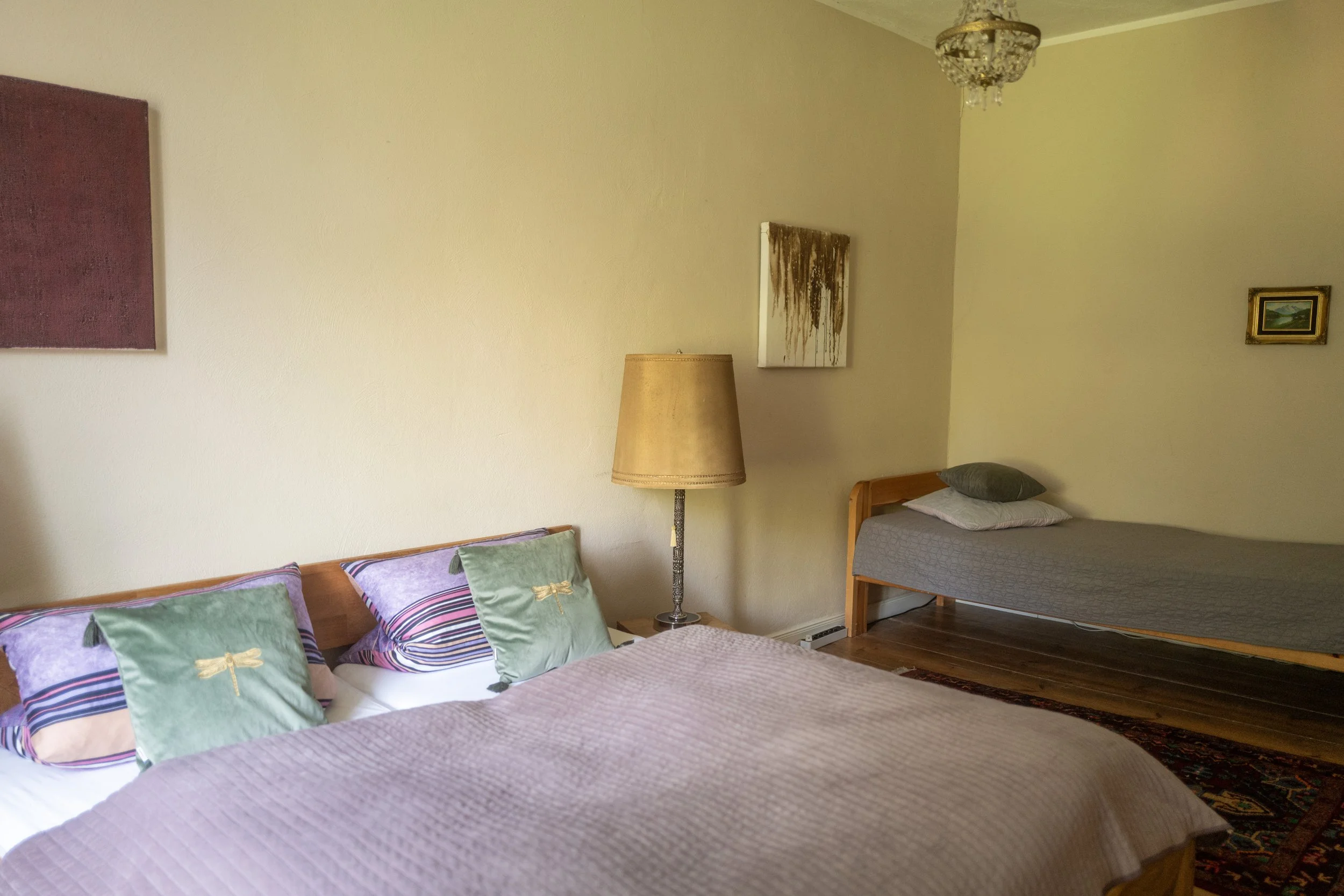 Ein Schlafzimmer mit zwei Betten, einem Stehlampe, Wandkunst und Holzboden.