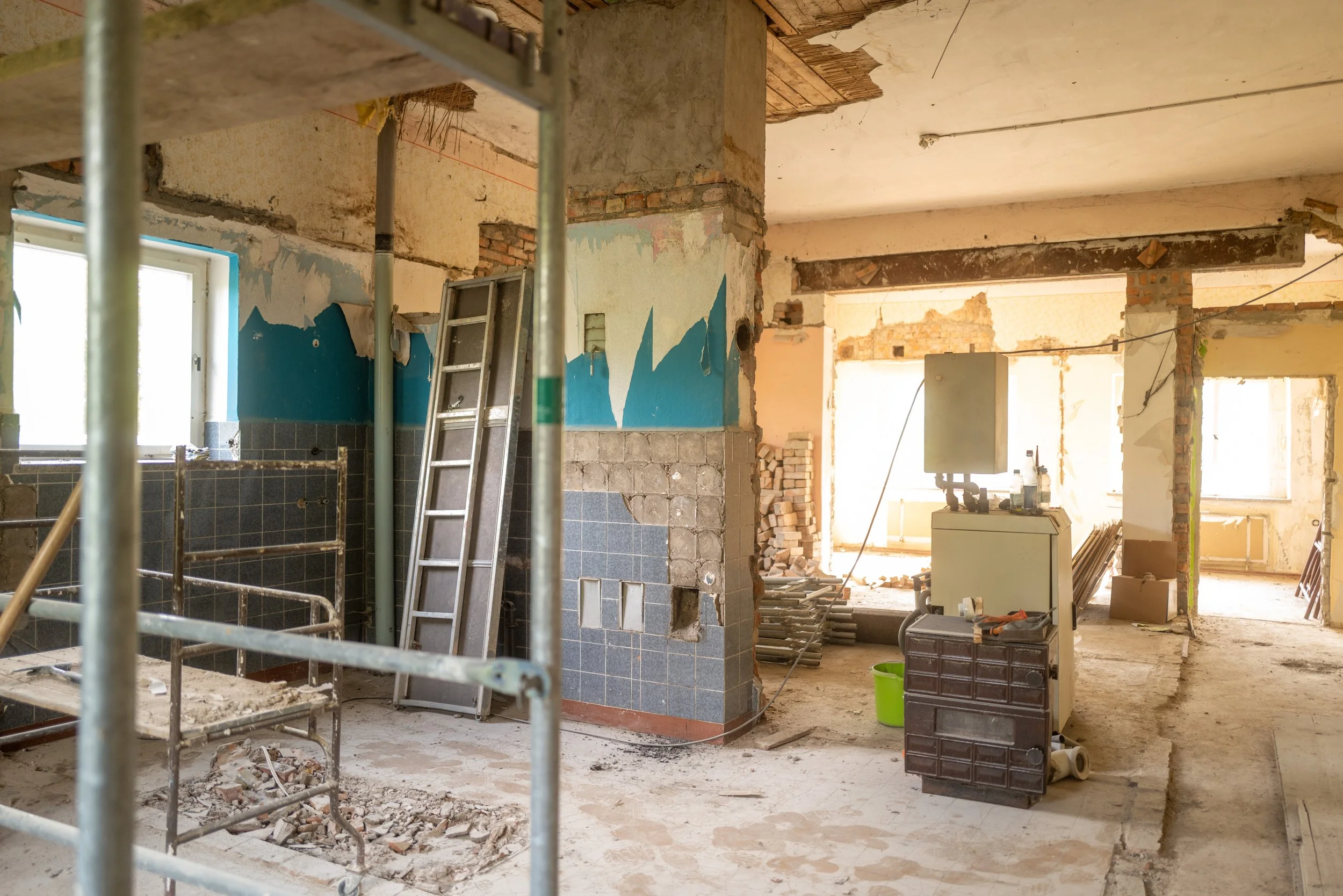 Innenraum eines renovierungsbedürftigen Hauses mit sichtbaren Ziegelwänden, Baugerüsten, Baustoffen und einem Fenster.