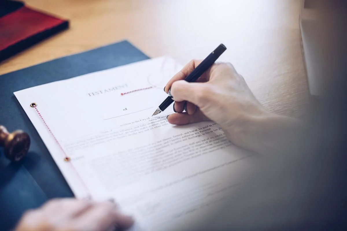 Person signing a legal document or contract on a wooden table.